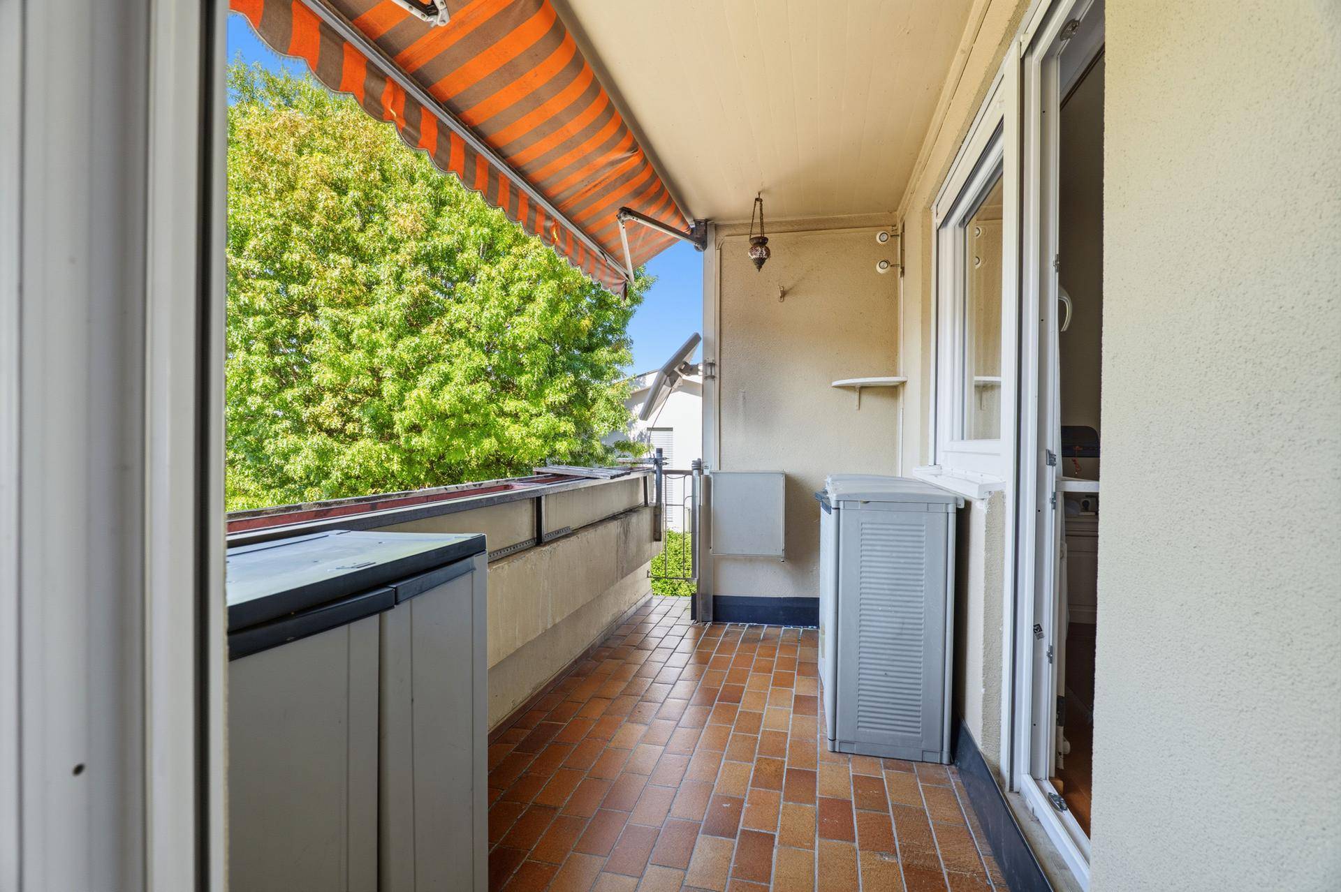Überdachter Balkon mit Markise, Fliesenboden und Blick ins Grüne.