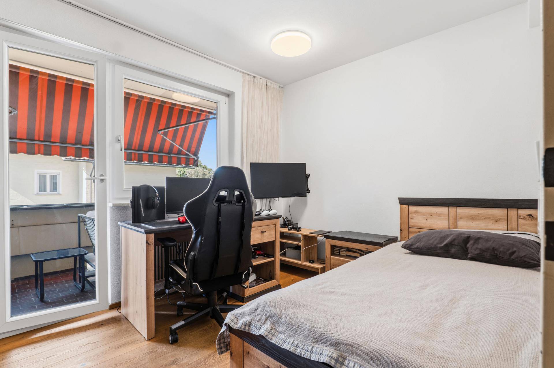 Jugendzimmer mit Schreibtisch, Gaming-Setup und Zugang zum Balkon.