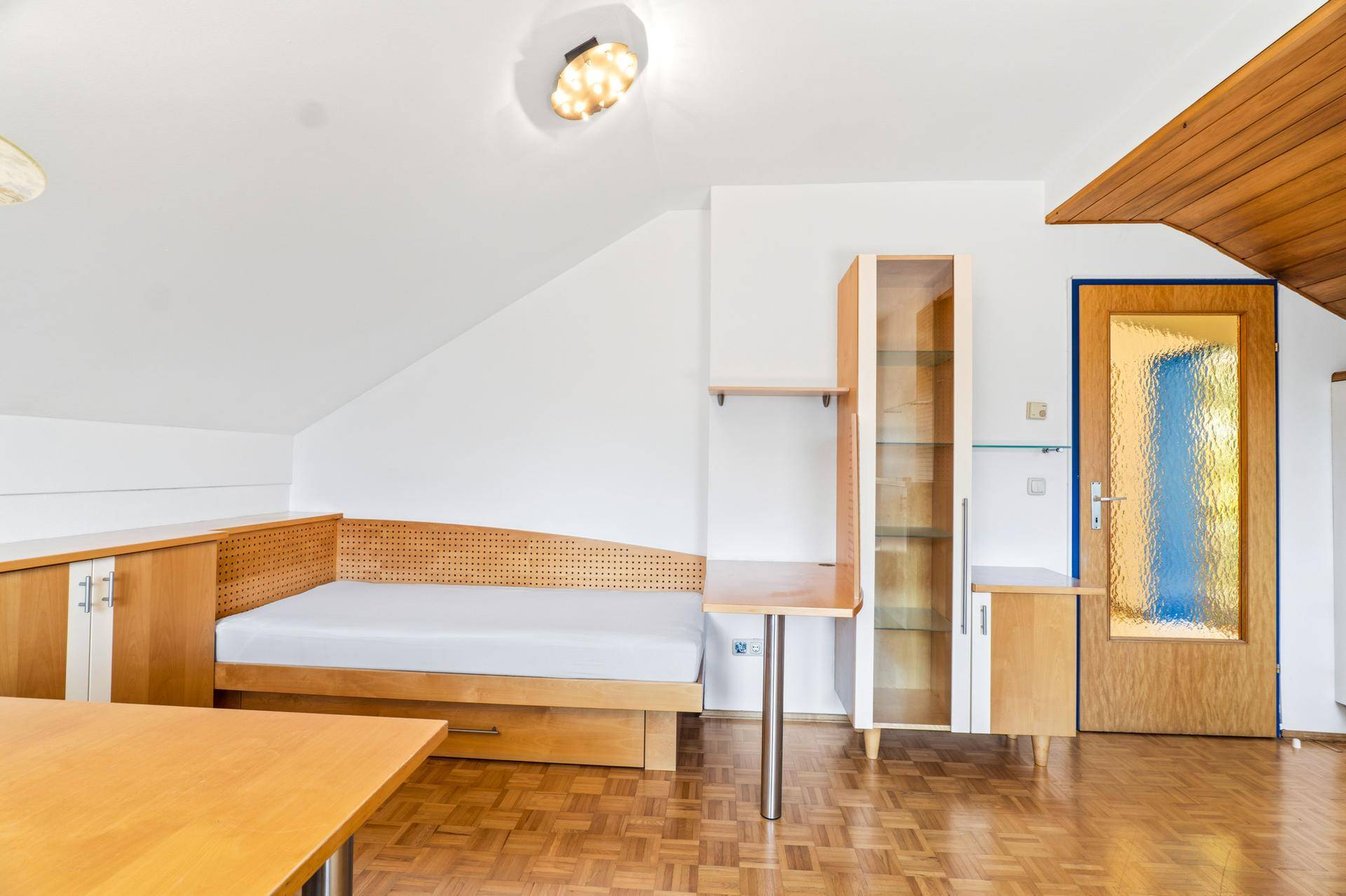Schlaf- oder Wohnbereich mit Holzboden, Dachschräge und praktischen Einbaumöbeln.