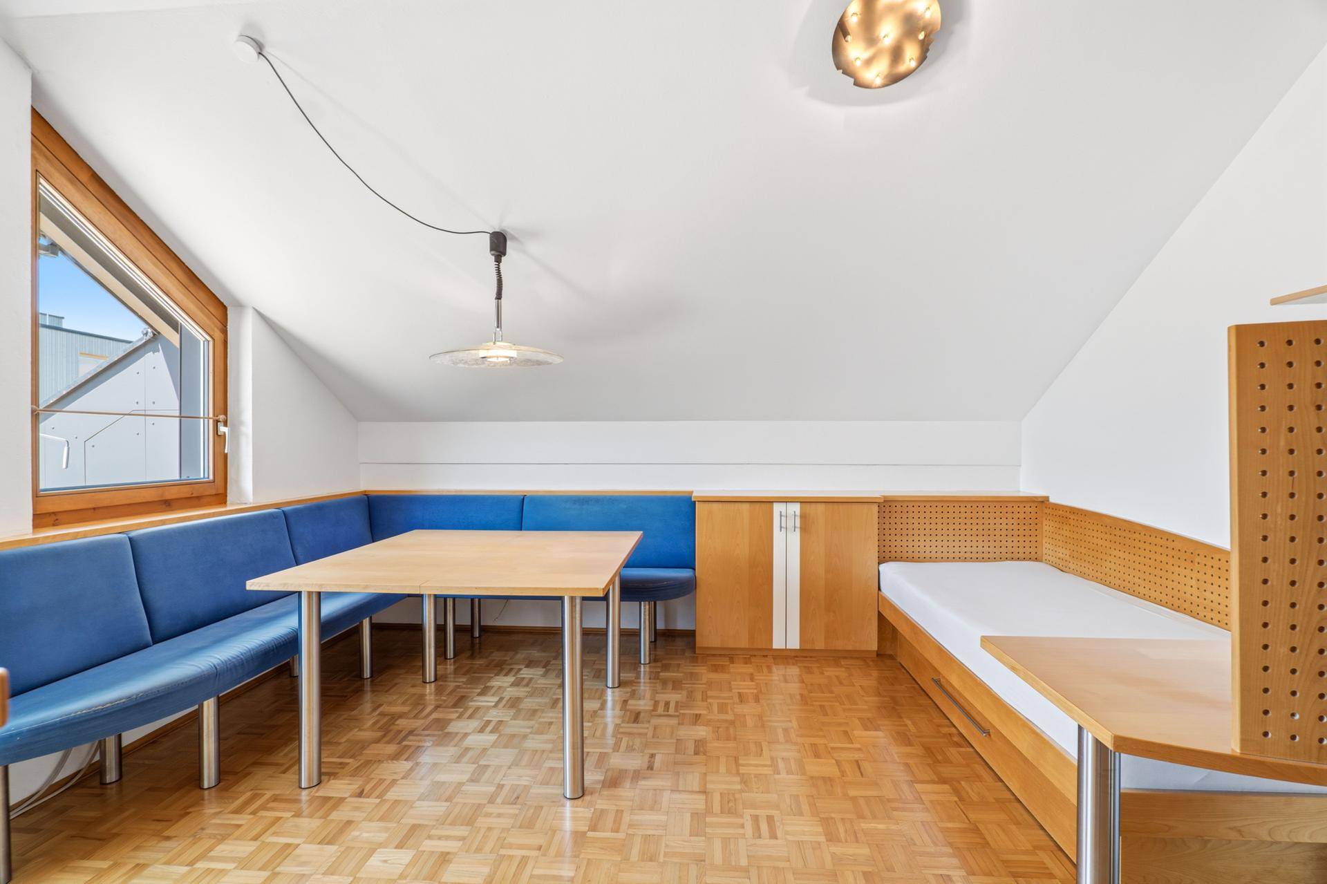 Vielseitiger Wohnraum mit Essbereich, Schlafgelegenheit und Holzboden unter Dachschrägen.