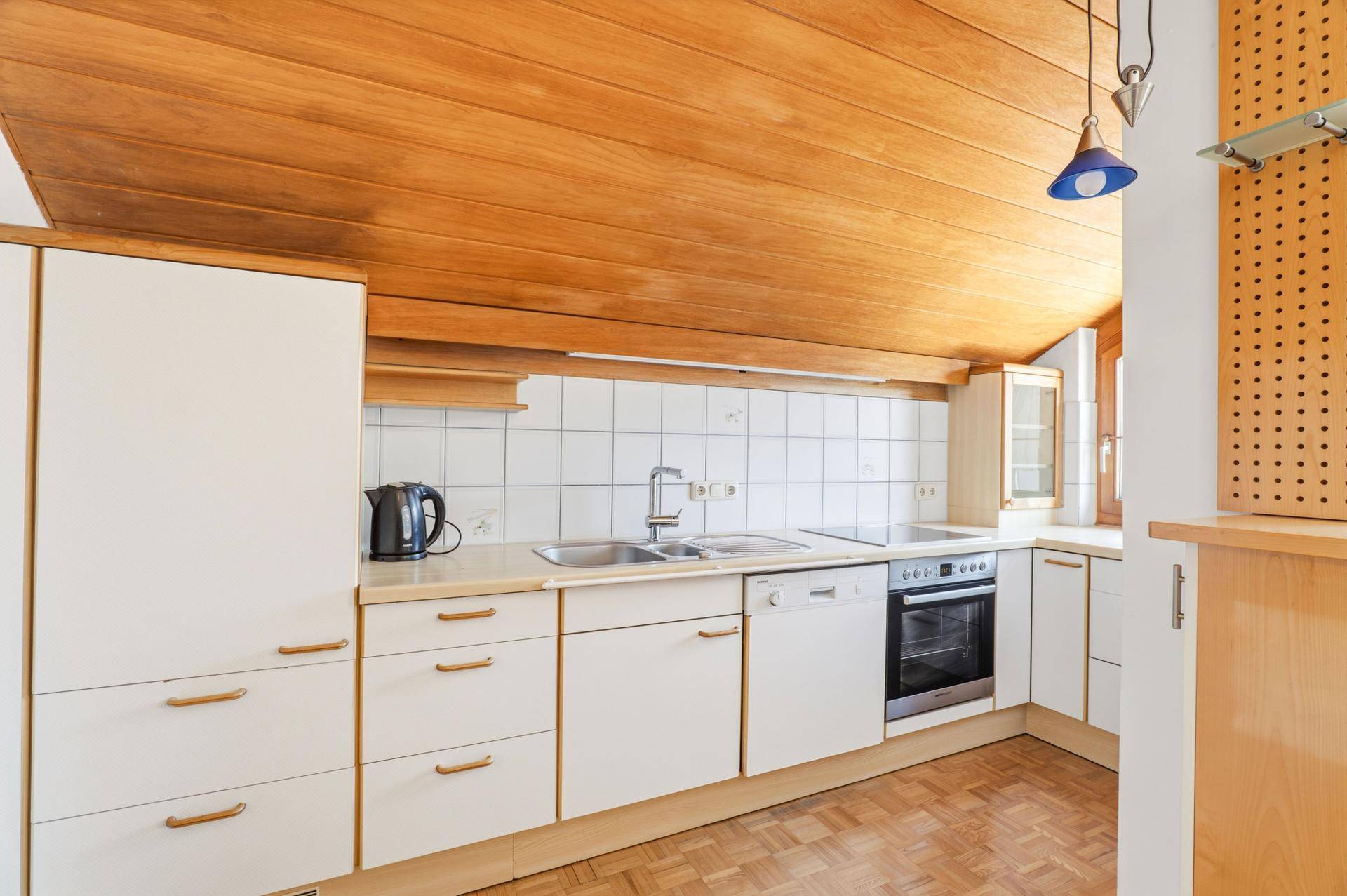 Kompakte Küche mit Holzdecke, weißen Fronten, integrierten Geräten und Parkettboden.