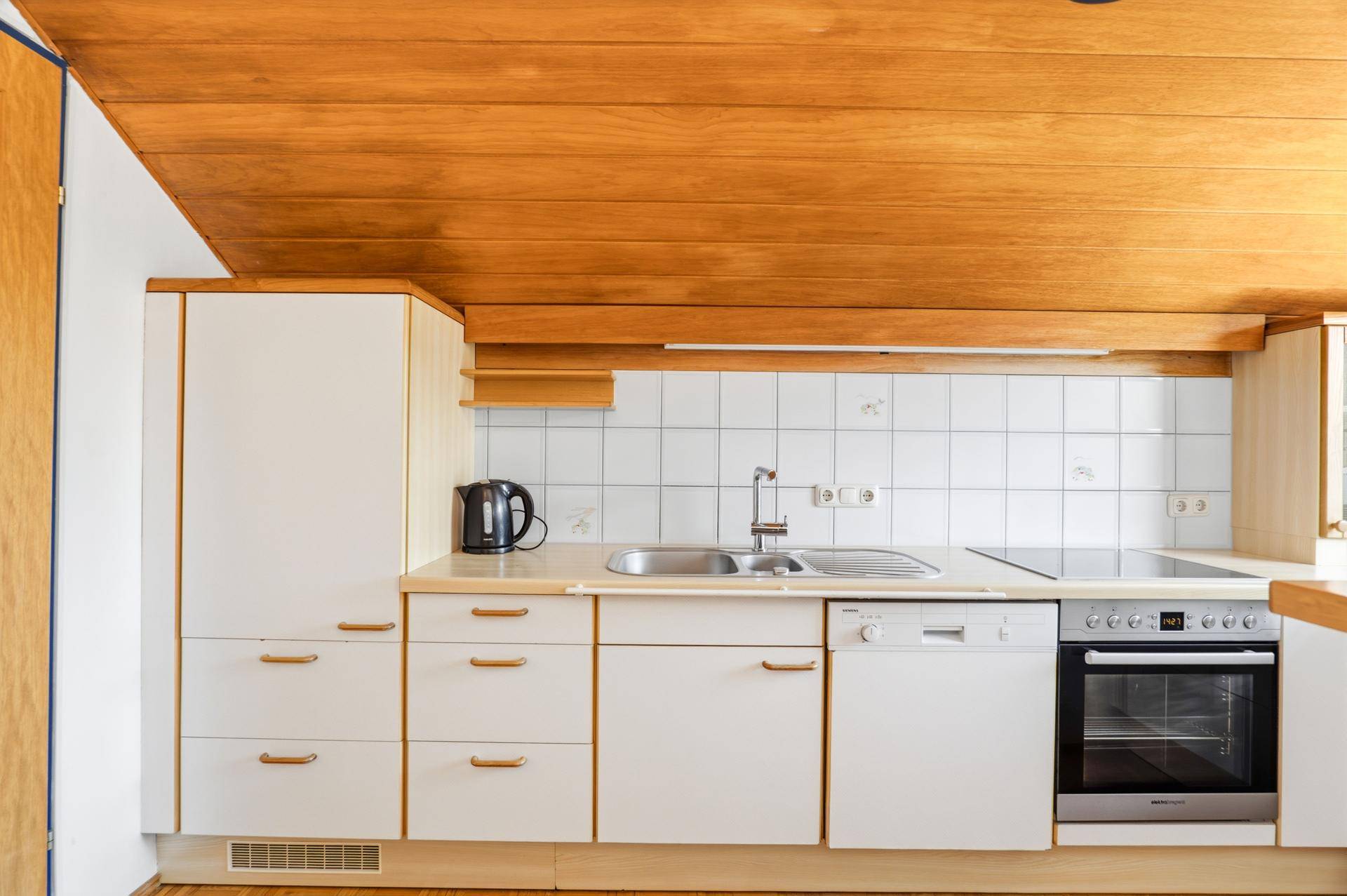 Funktionale Küche mit weißen Schränken, Holzdecke, Fliesenrückwand und integrierten Geräten.
