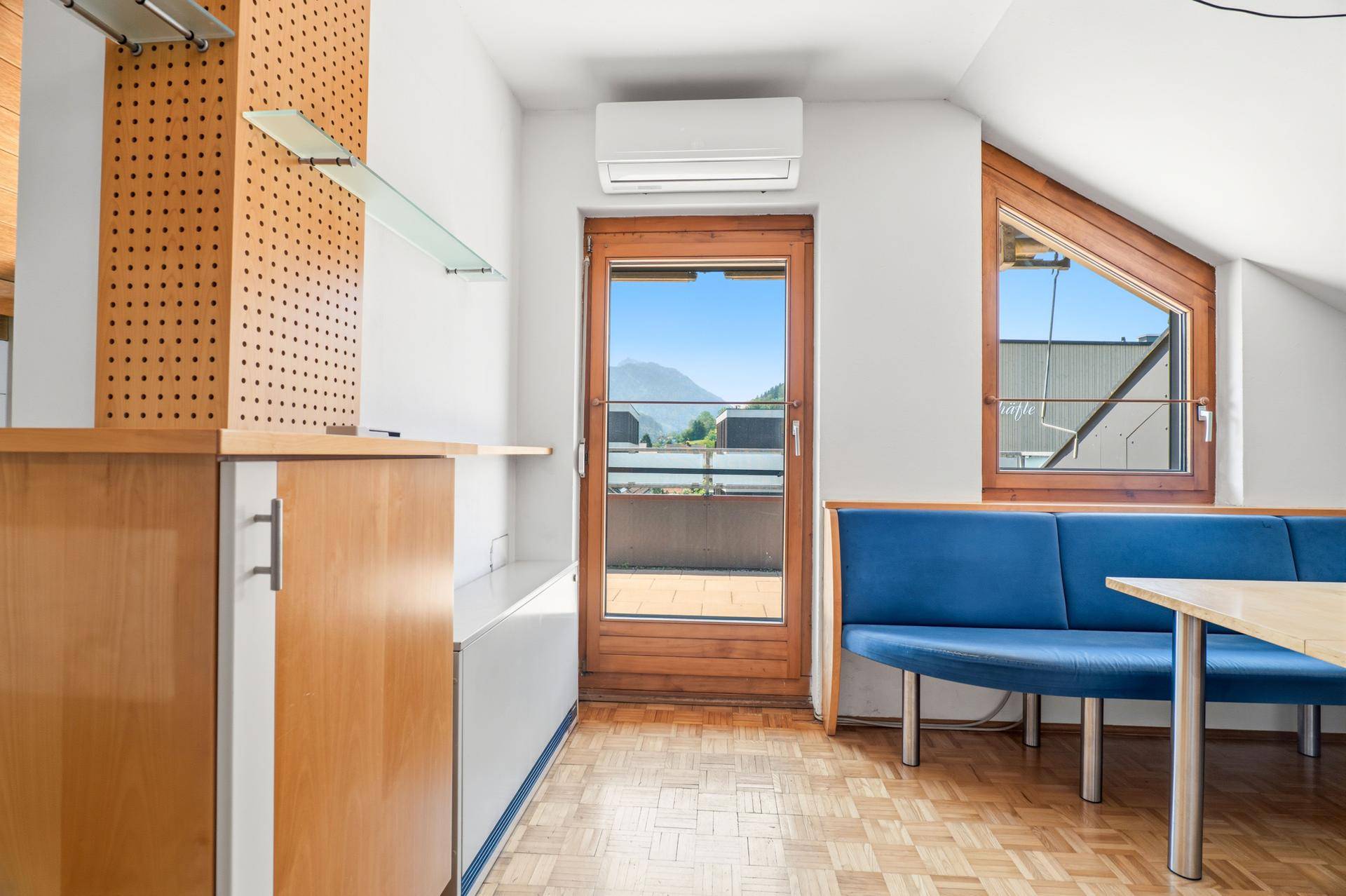 Heller Wohnbereich mit Zugang zur Dachterrasse und Blick auf die umliegenden Berge.