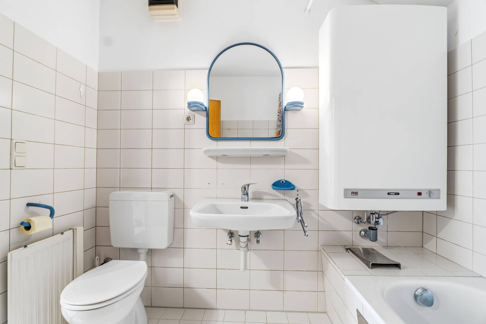 Helles Badezimmer mit WC, Waschbecken und weiß gefliesten Wänden.