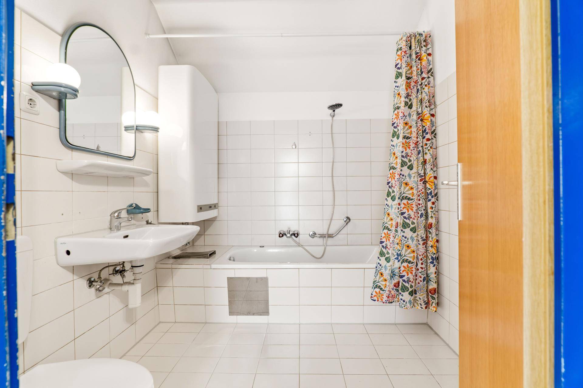 Funktionales Badezimmer mit Badewanne, Waschbecken und weißen Wand- und Bodenfliesen.