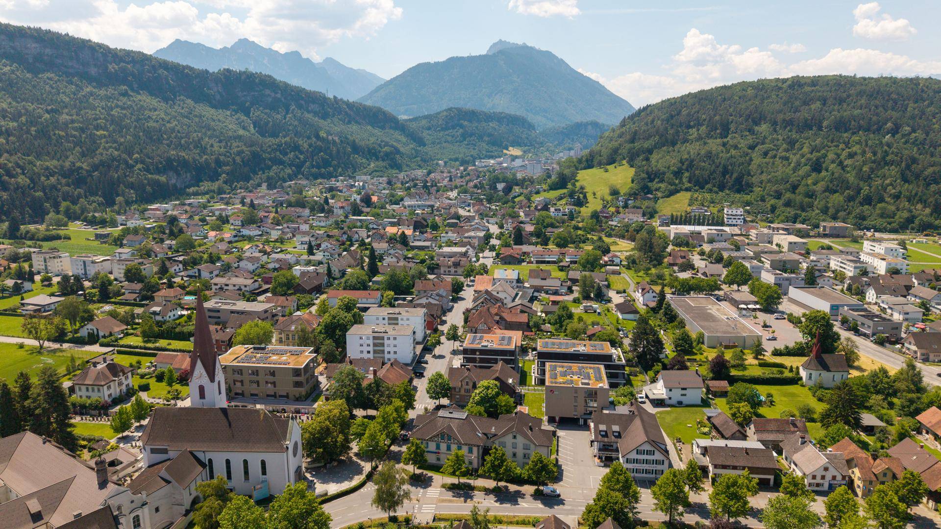 Weitläufige Luftaufnahme einer Stadt in einem Tal, umgeben von grünen Bergen.