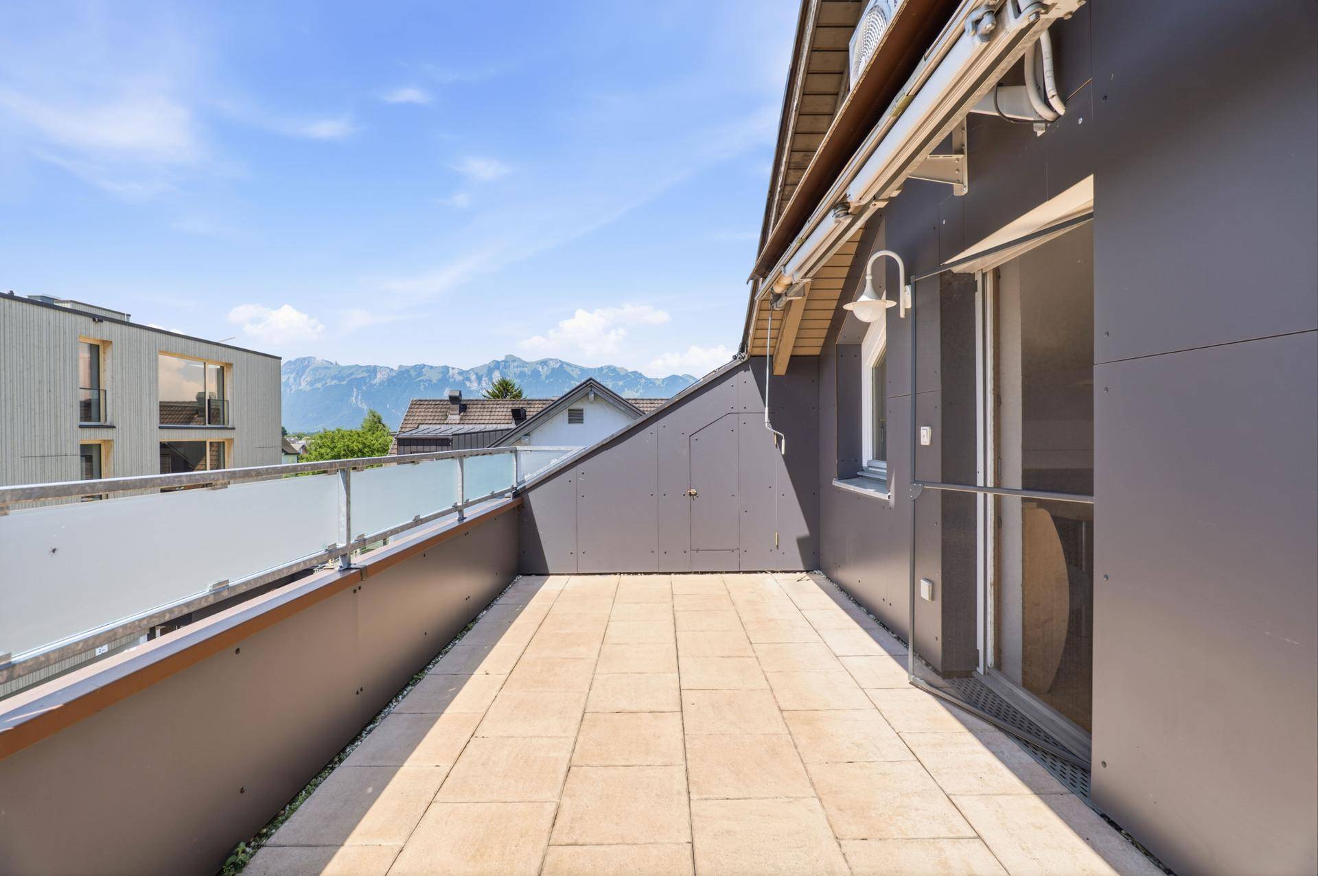 Großzügige Dachterrasse mit Fliesenboden, Glasgeländer und Bergblick.