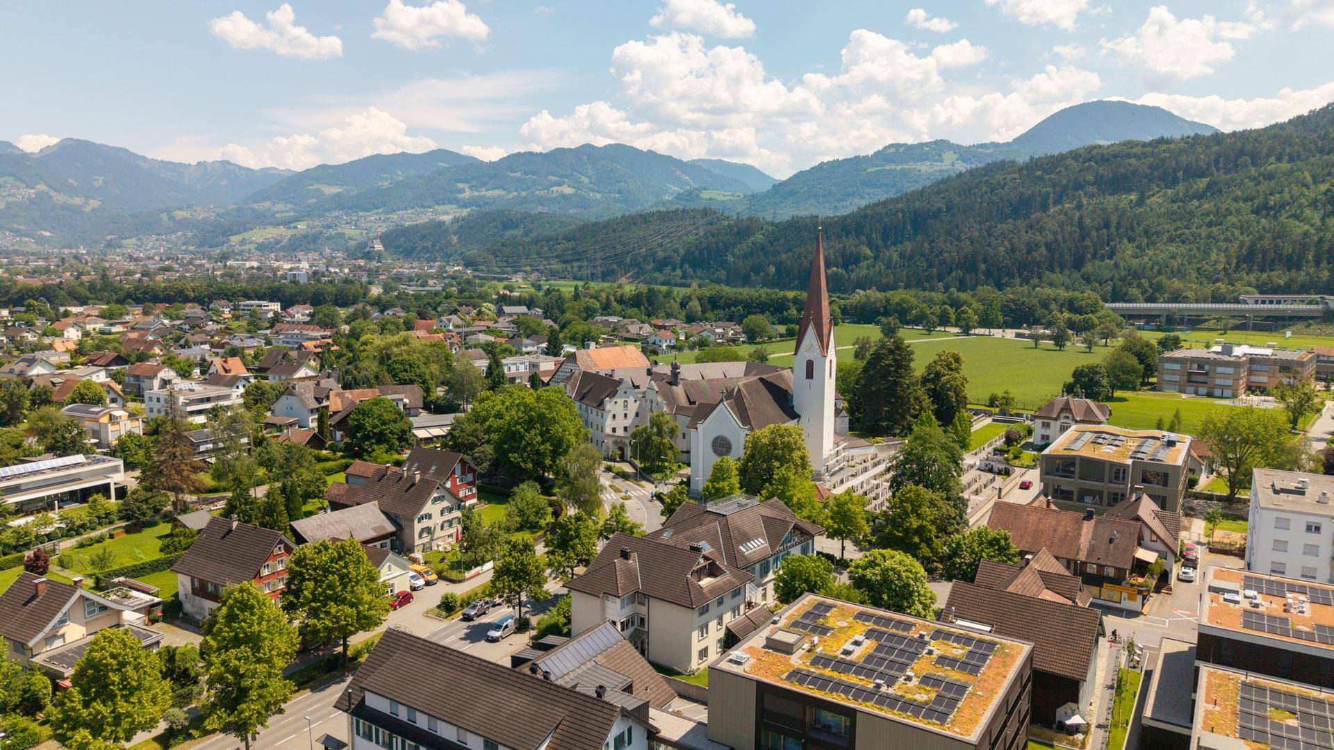 Panoramablick aus der Vogelperspektive auf eine Stadt mit Bergen im Hintergrund.