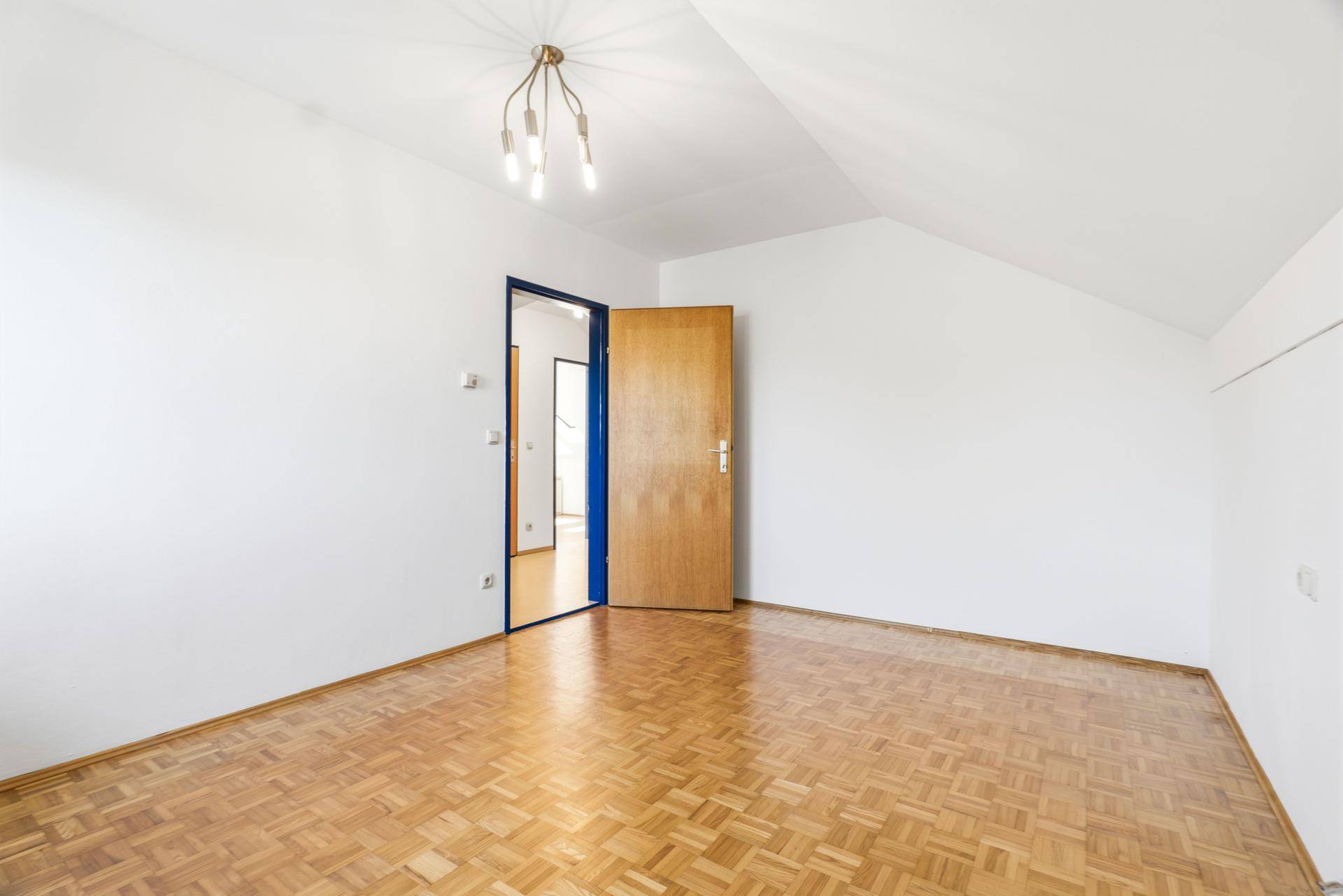 Geräumiges Schlafzimmer mit Holzboden, weiß gestrichenen Wänden und Holztür.