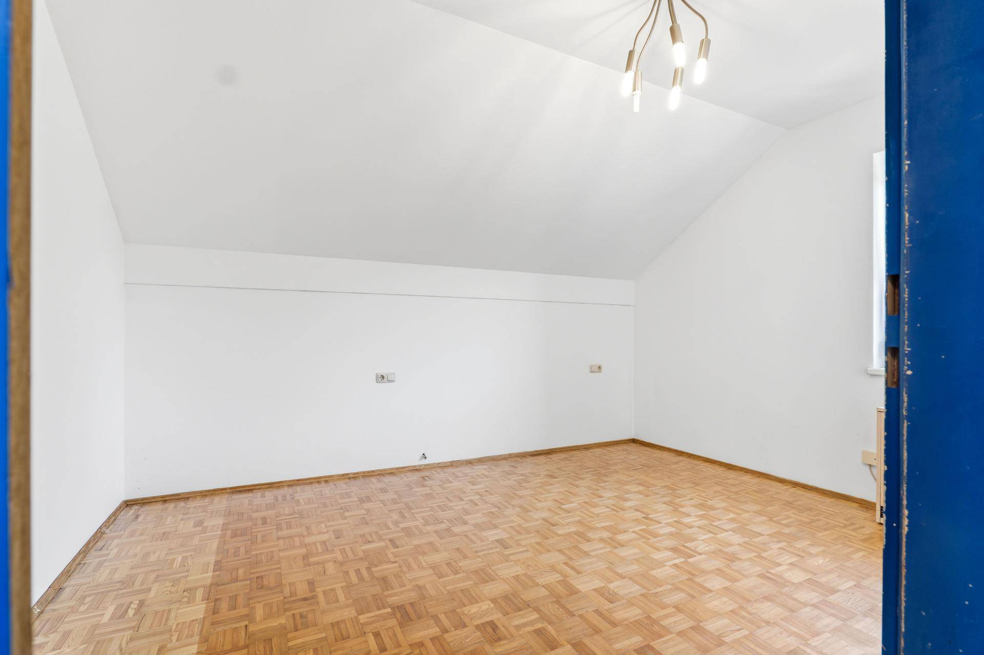 Leeres Schlafzimmer mit Holzboden, weißen Wänden und charakteristischer Dachschräge.