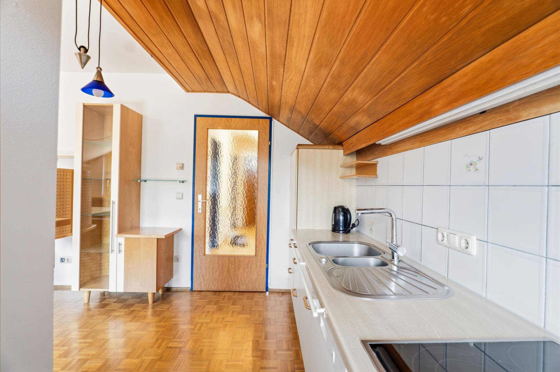 Küche mit Holzdecke, weißen Schränken und Zugang zu weiteren Räumen.