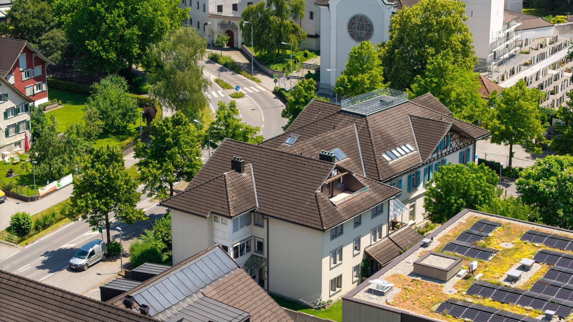 Luftaufnahme eines Wohngebiets mit Häusern, grünen Bäumen und Straßennetz.