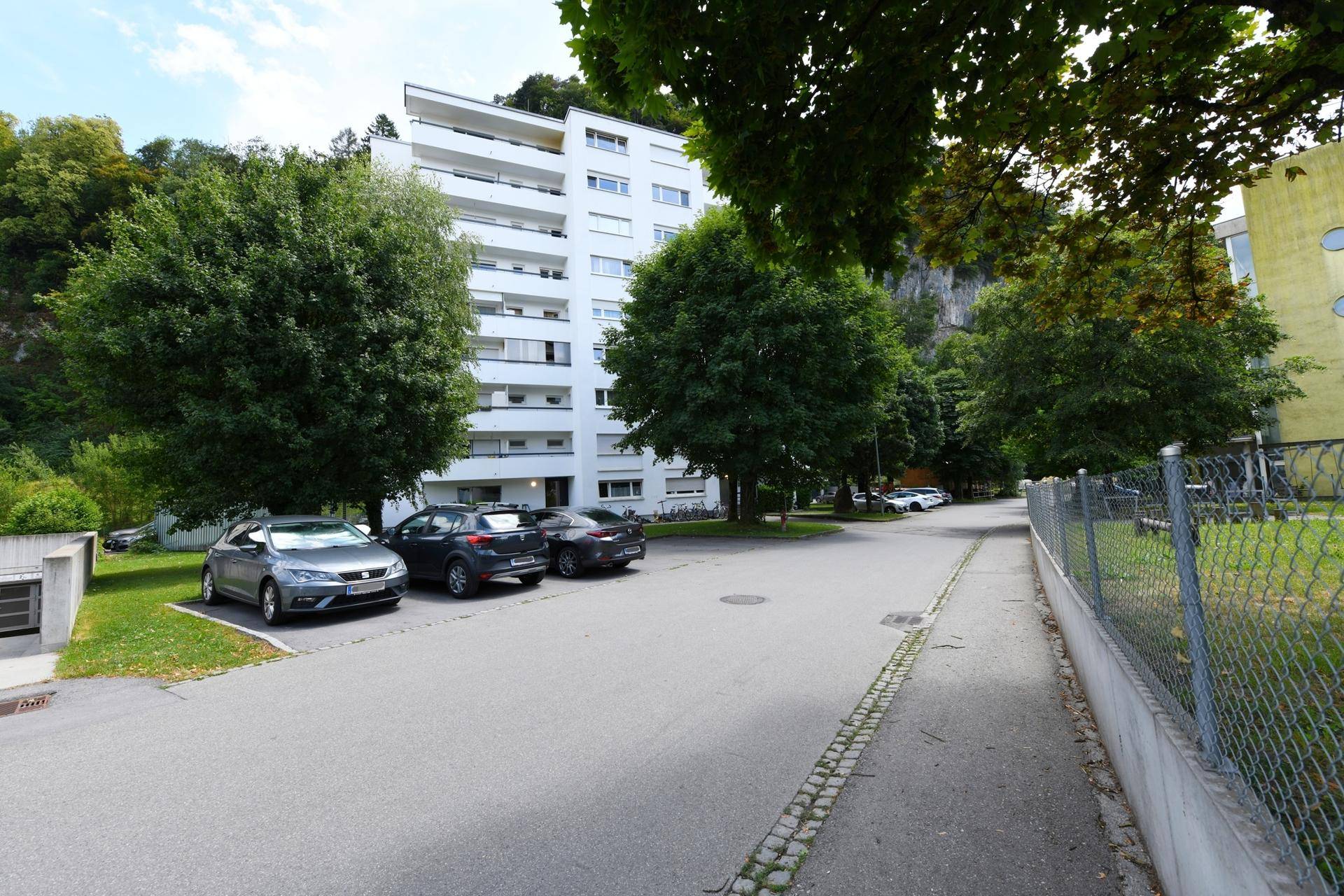 Mehrstöckiges weißes Wohngebäude umgeben von Bäumen und Parkplätzen.