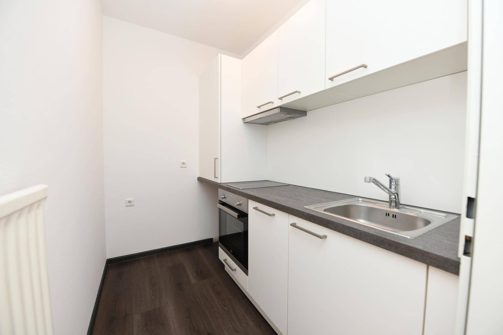 Kleine, moderne Küche mit weißen Schränken, dunkler Arbeitsplatte und integrierten Geräten.