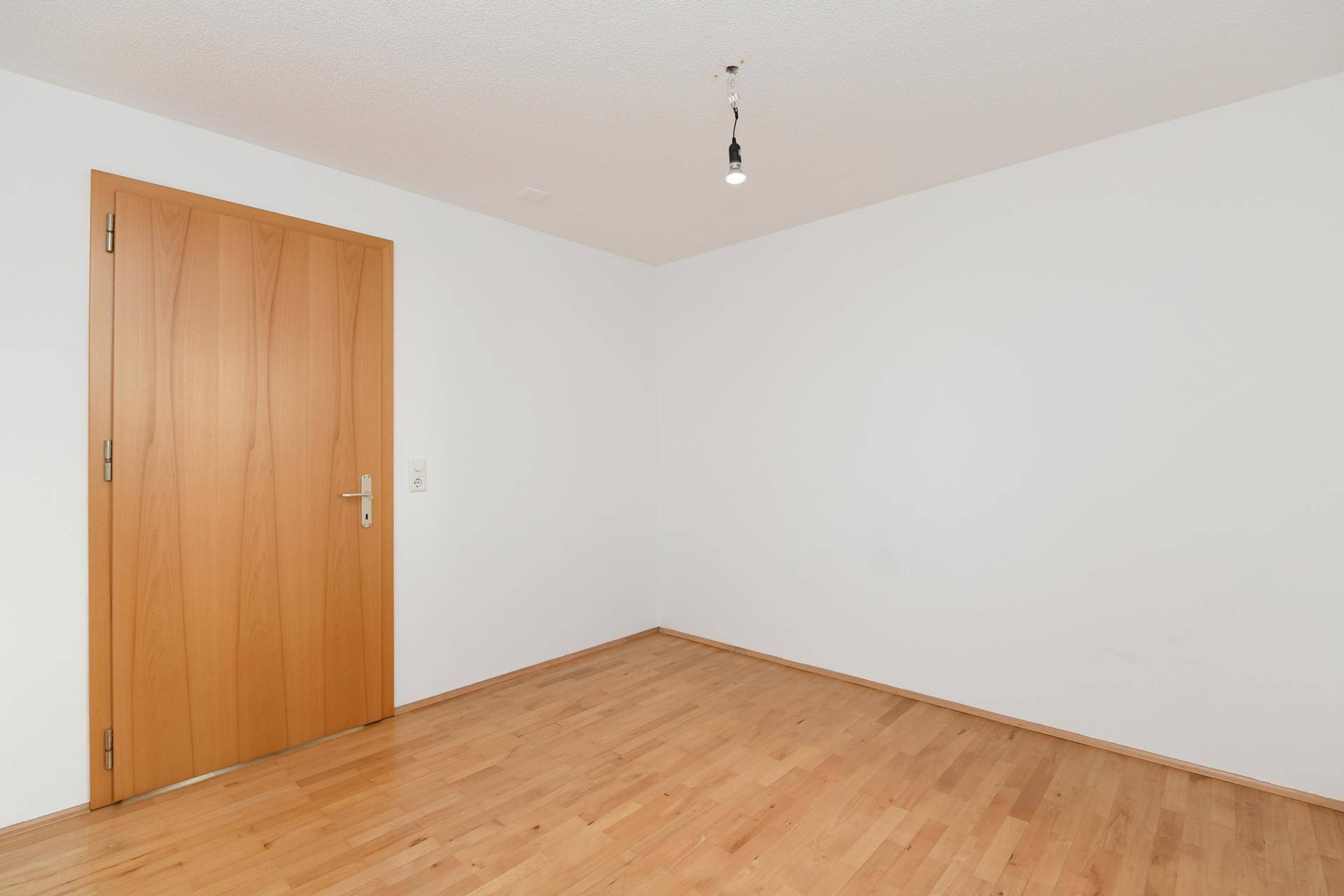 Leeres Zimmer mit hellem Holzboden und einer Holztür, bereit zur individuellen Gestaltung.