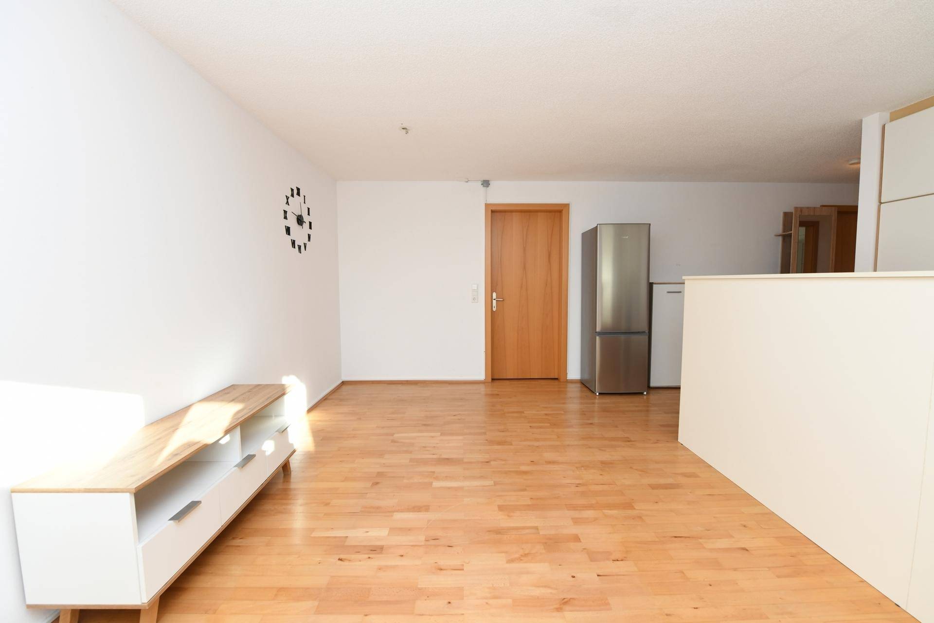 Leerer Wohnbereich mit hellem Holzboden und schlichtem TV-Möbel.