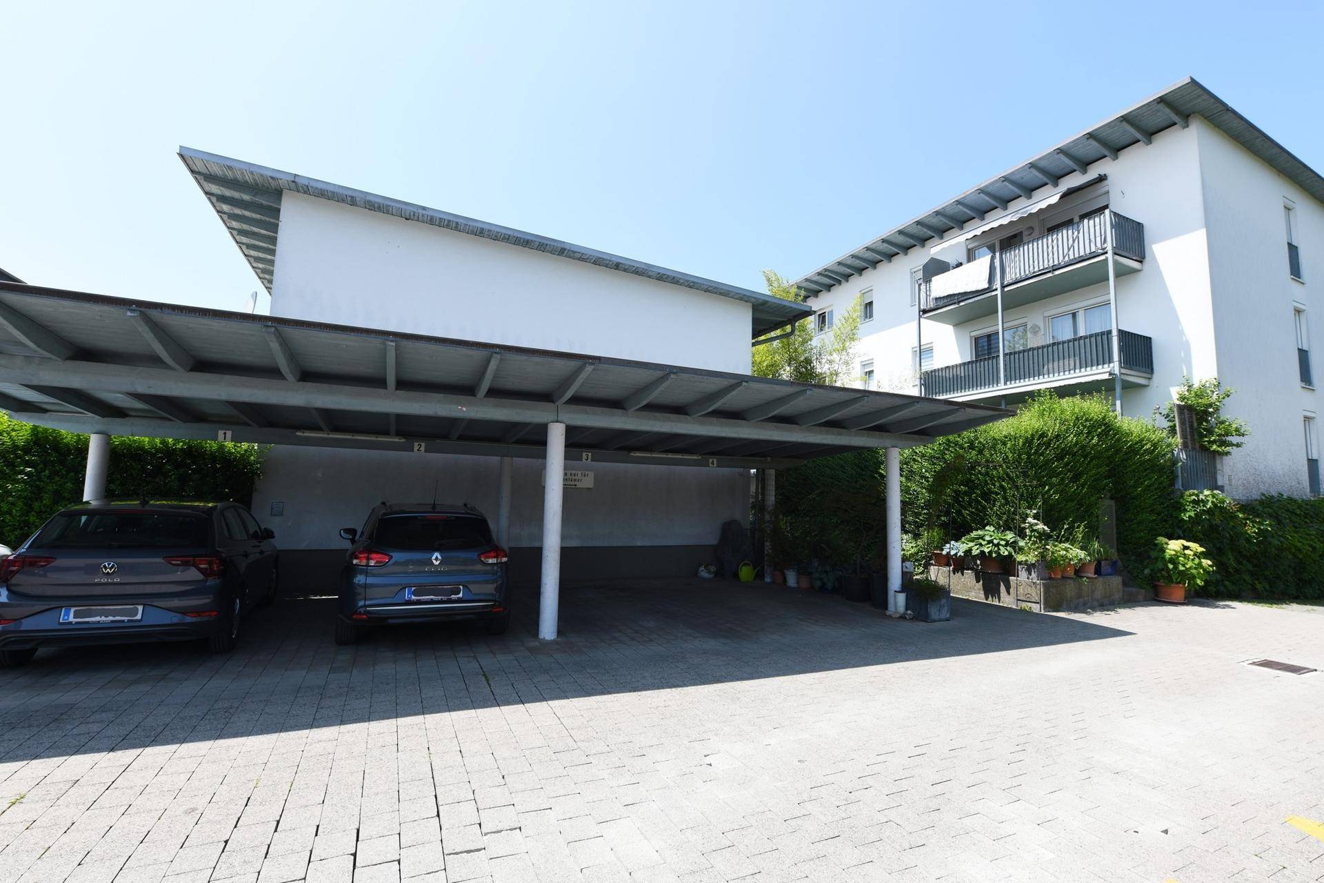 Überdachter Carport mit zwei Stellplätzen vor einem Mehrfamilienhaus.