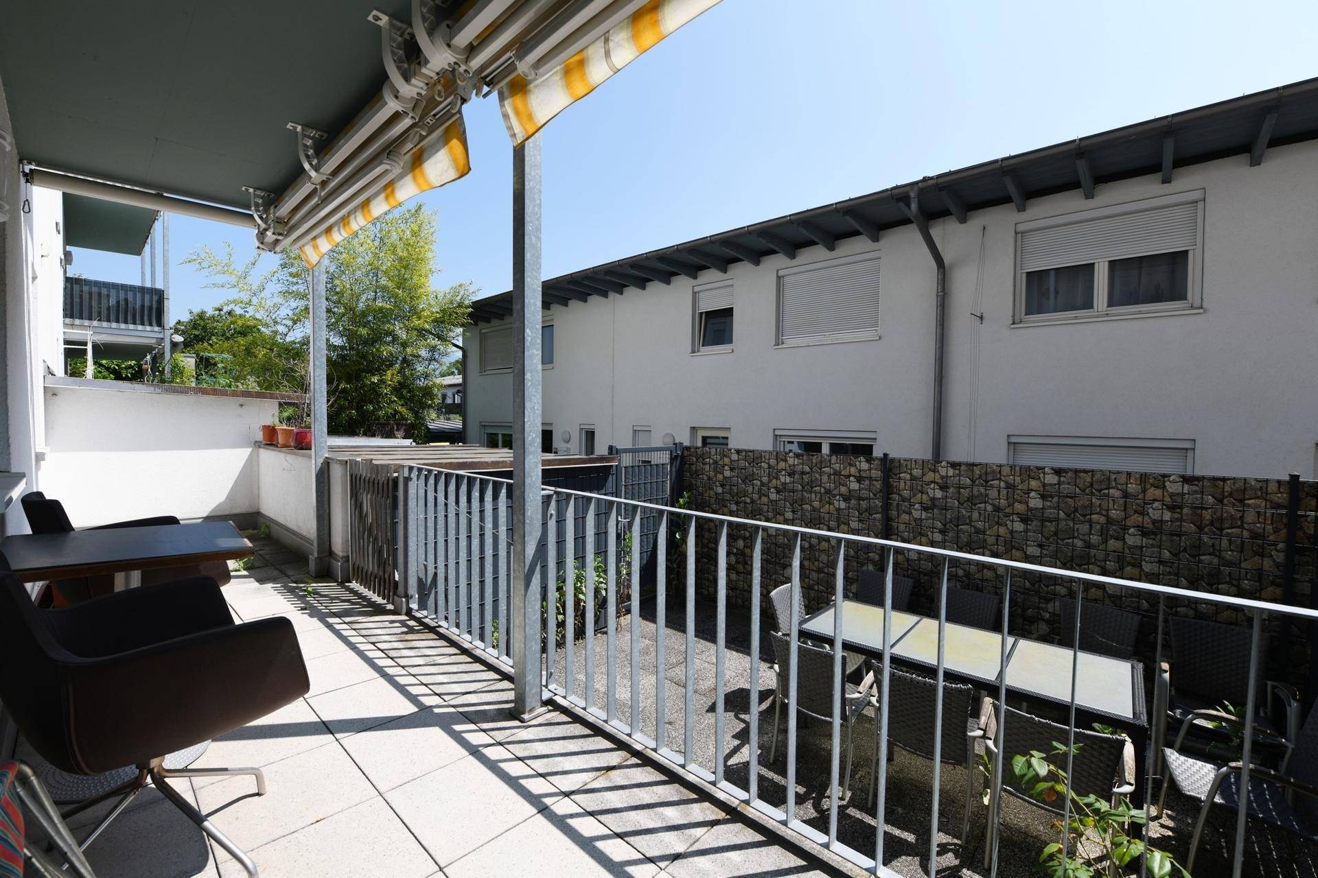 Sonniger Balkon mit Fliesenboden, Gartenmöbeln und Blick auf die Umgebung.