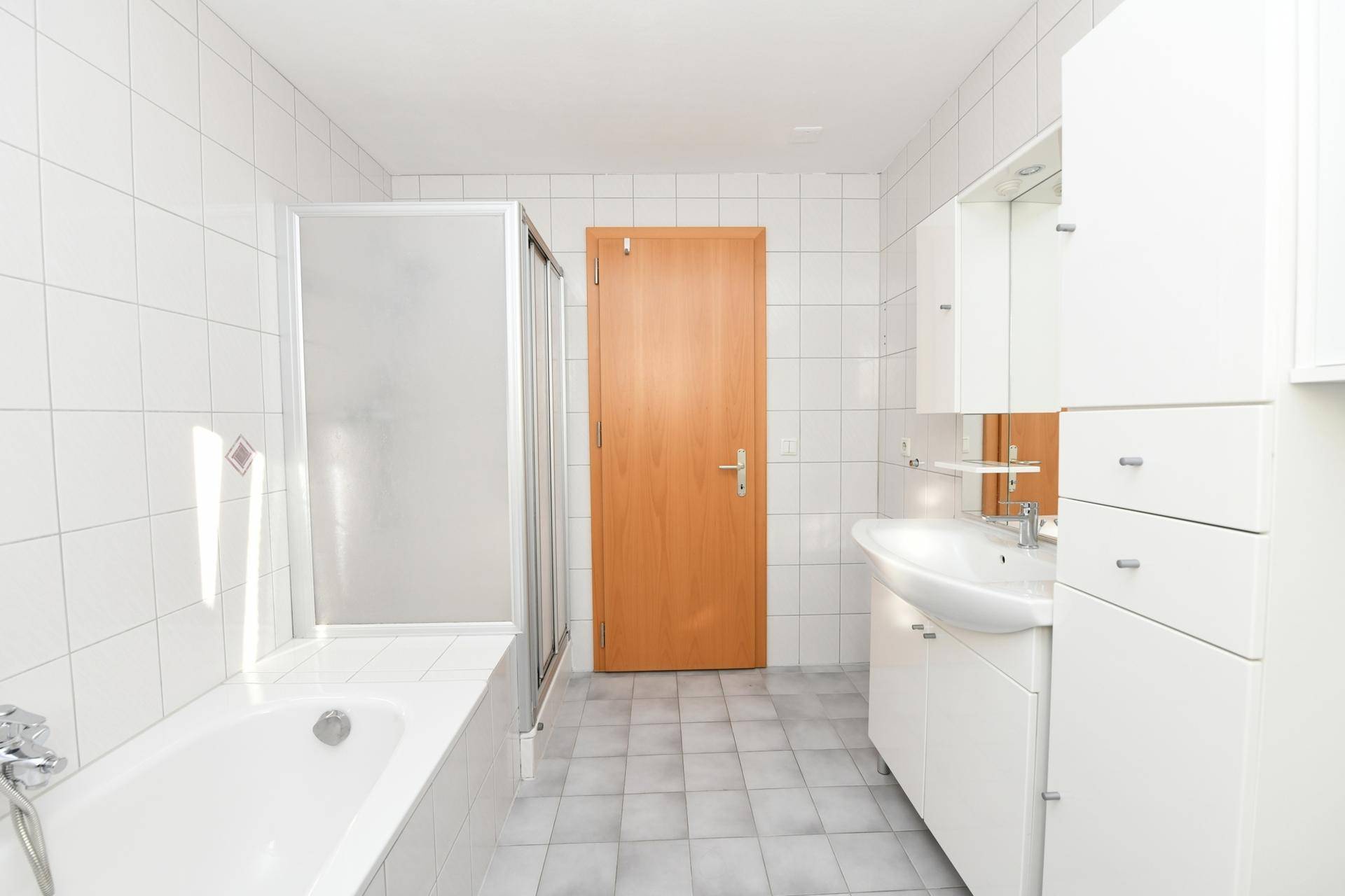 Badezimmer mit weißen Fliesen, Badewanne, Duschkabine und Waschbecken mit Unterschrank.