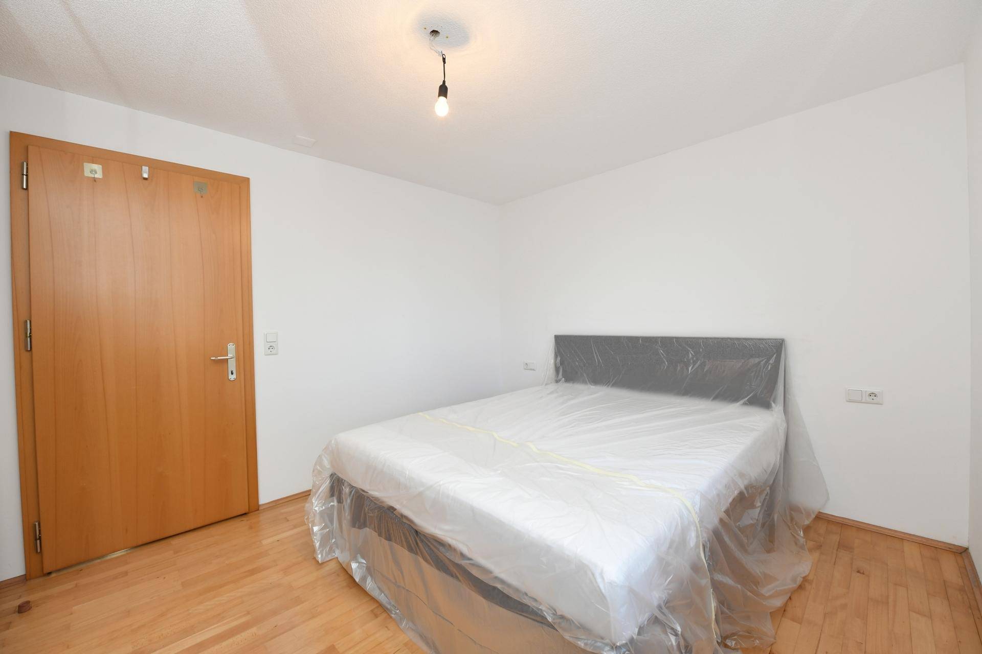 Schlafzimmer mit Holzboden, Holztür und einem Bett, das für den Transport vorbereitet ist.