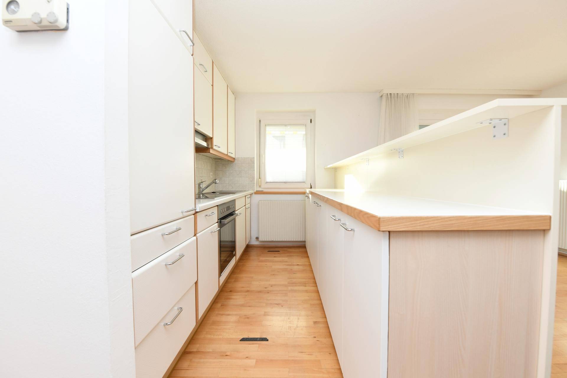 Funktionale Küche mit weißen Schränken, integriertem Backofen und Frühstückstheke.