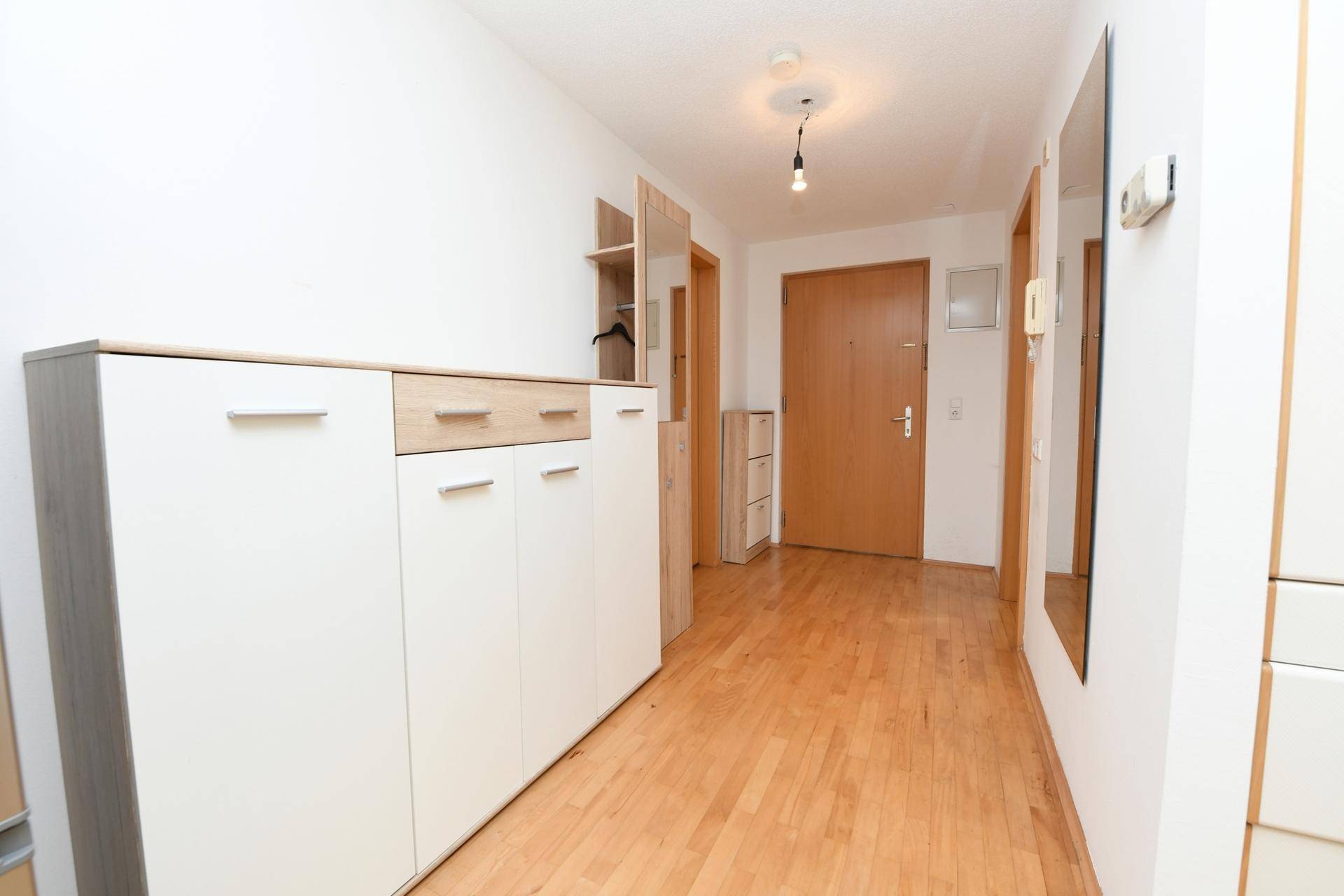 Heller Flur mit Holzboden, weiß gestrichenen Wänden und praktischem Schuhschrank.