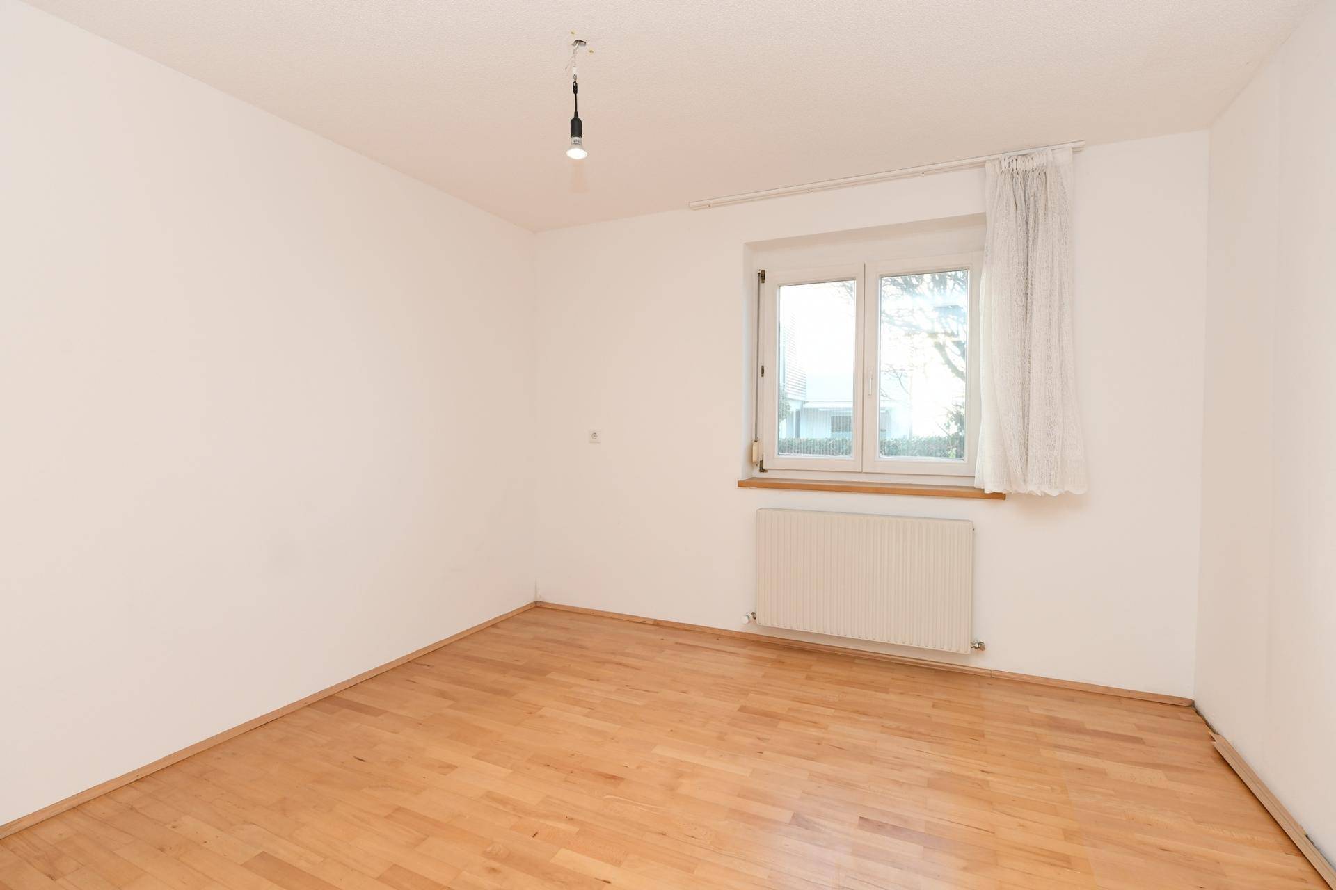 Leeres Zimmer mit hellem Holzboden und einem Fenster, ideal als Schlaf- oder Kinderzimmer.