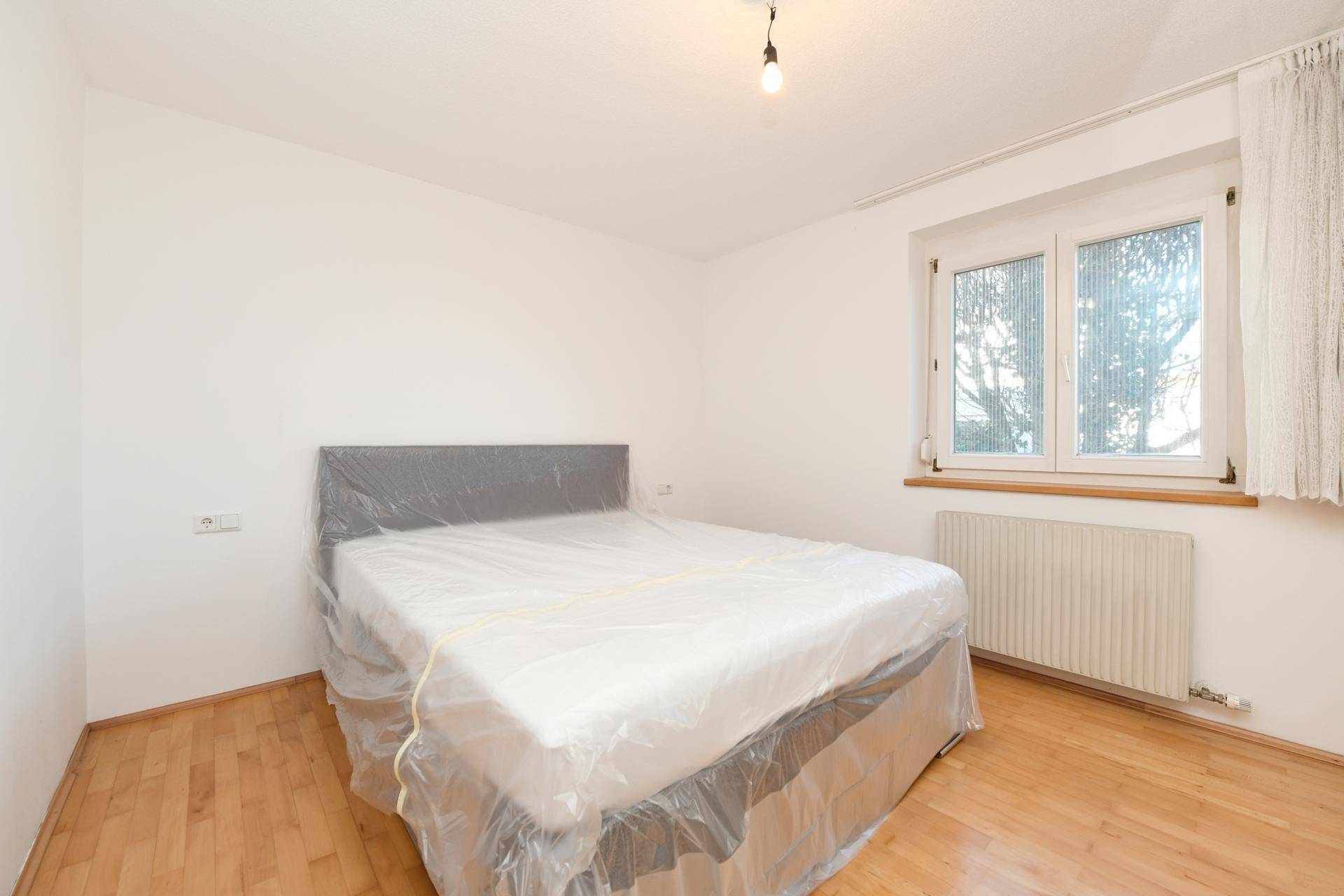 Schlafzimmer mit Holzboden, Fenster und einem Bett, das für den Transport vorbereitet ist.