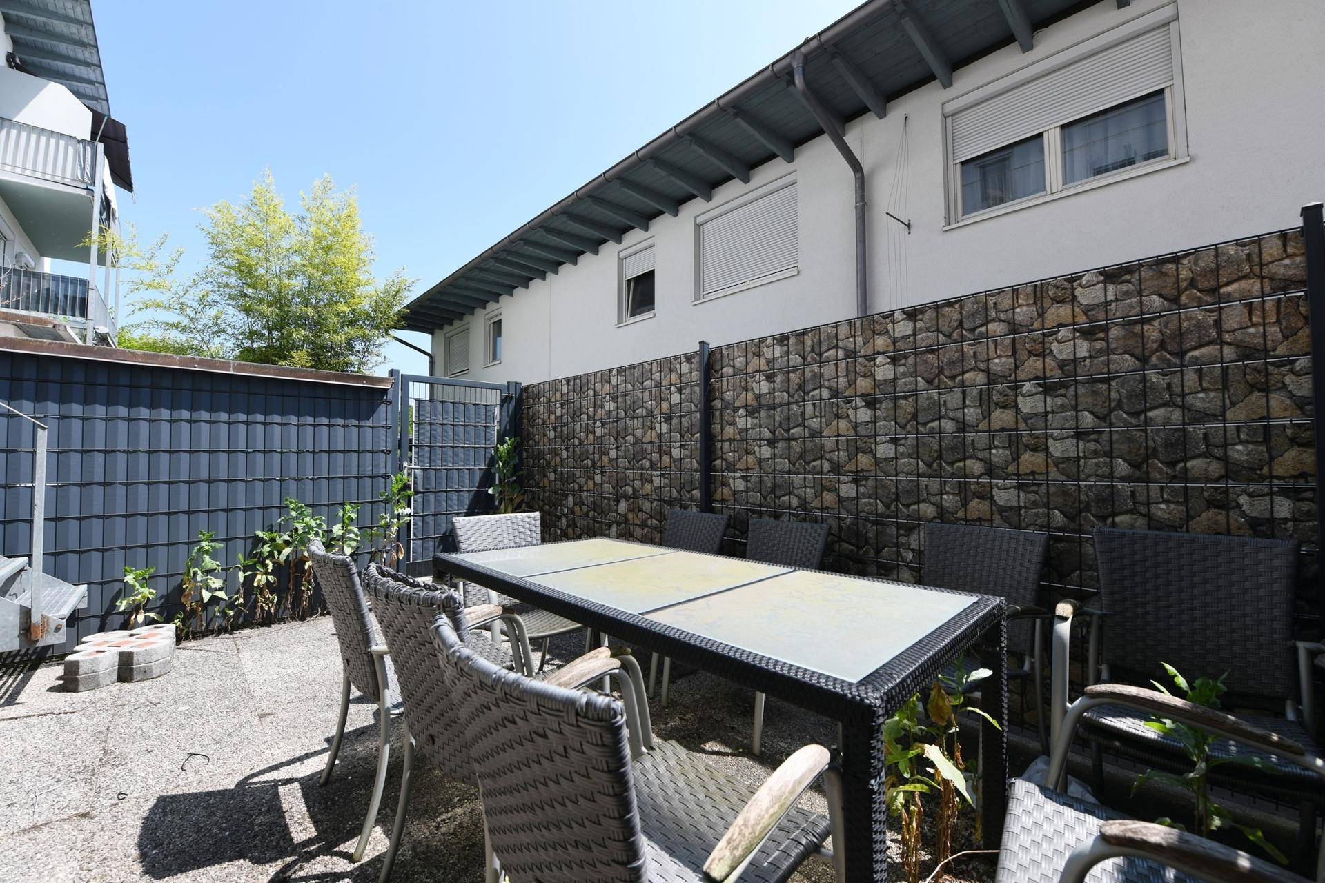 Gemütliche Terrasse mit Esstisch und Stühlen, umgeben von einer Gabionenwand.