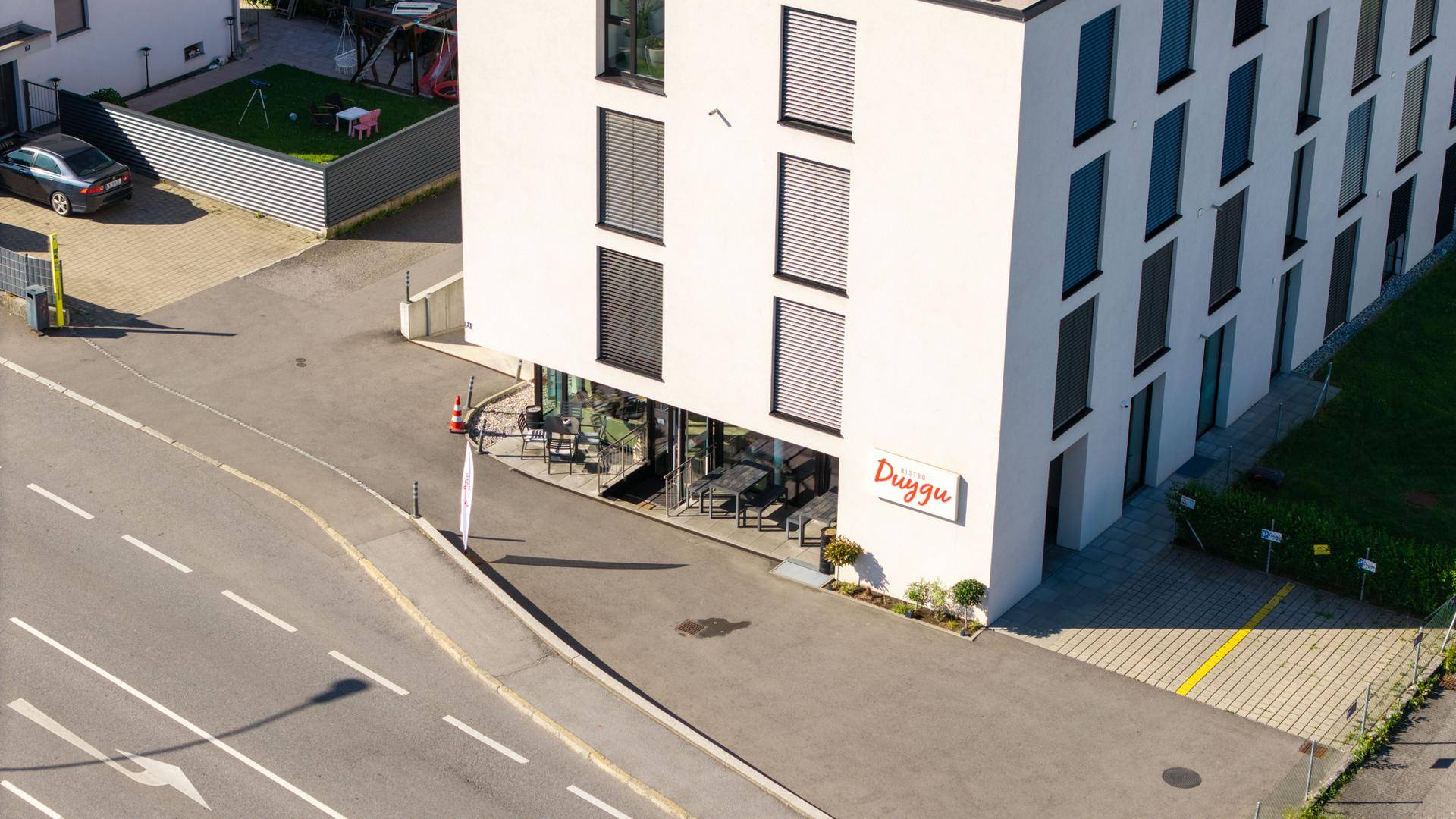 Luftaufnahme des modernen Geschäftsgebäudes mit Bistro und umliegenden Straßen und Parkplätzen.