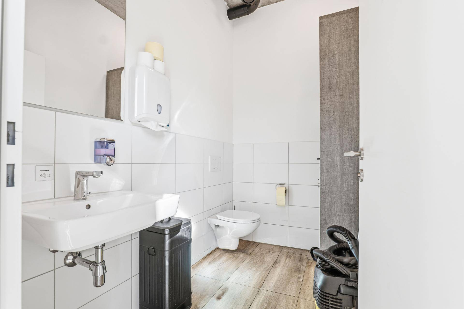 Saubere Toilette mit modernem Waschbecken, Wand-WC und weißen Fliesen an den Wänden.