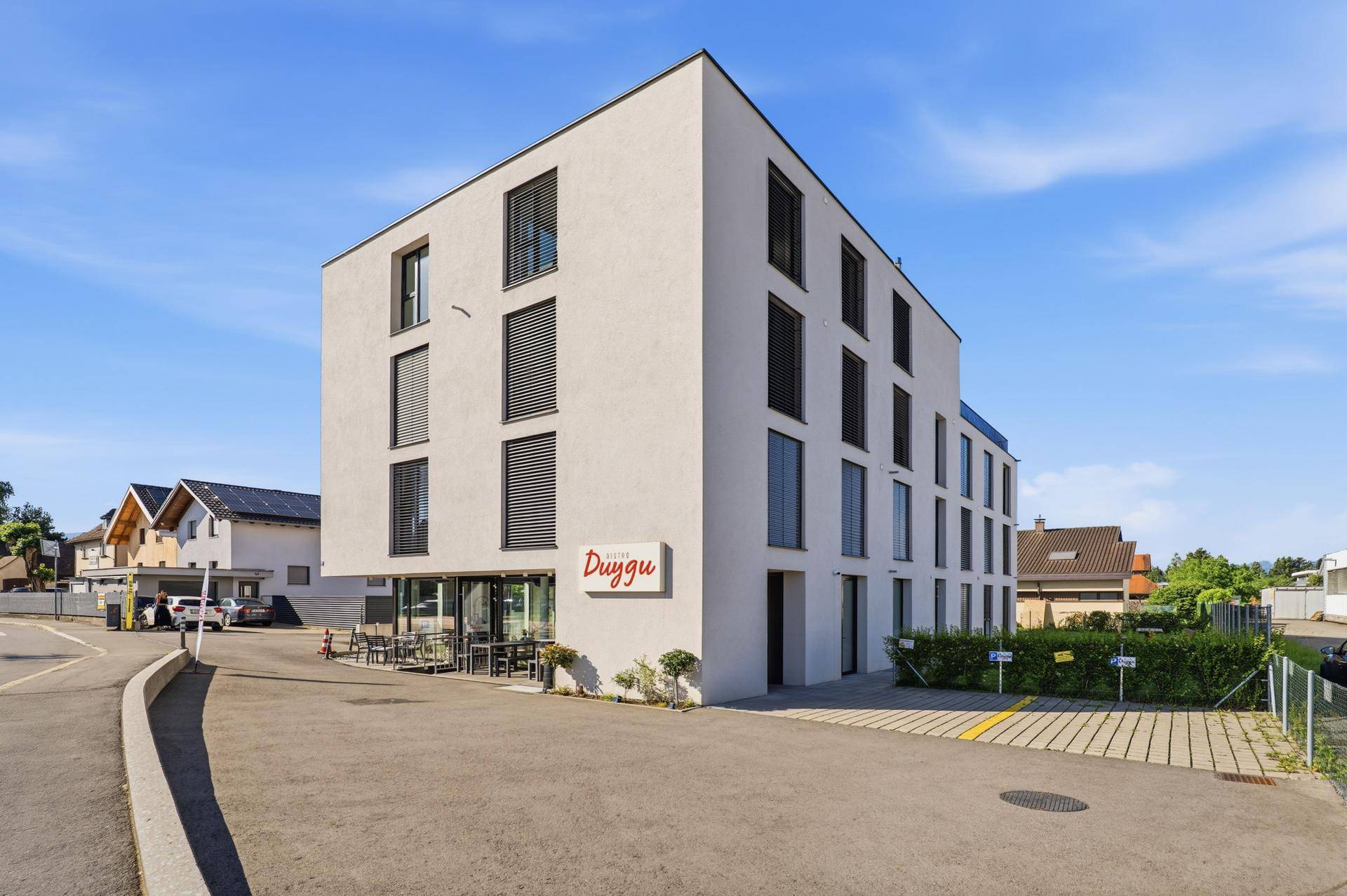 Gesamtansicht des modernen Geschäftsgebäudes mit Bistro im Erdgeschoss und Parkplätzen.