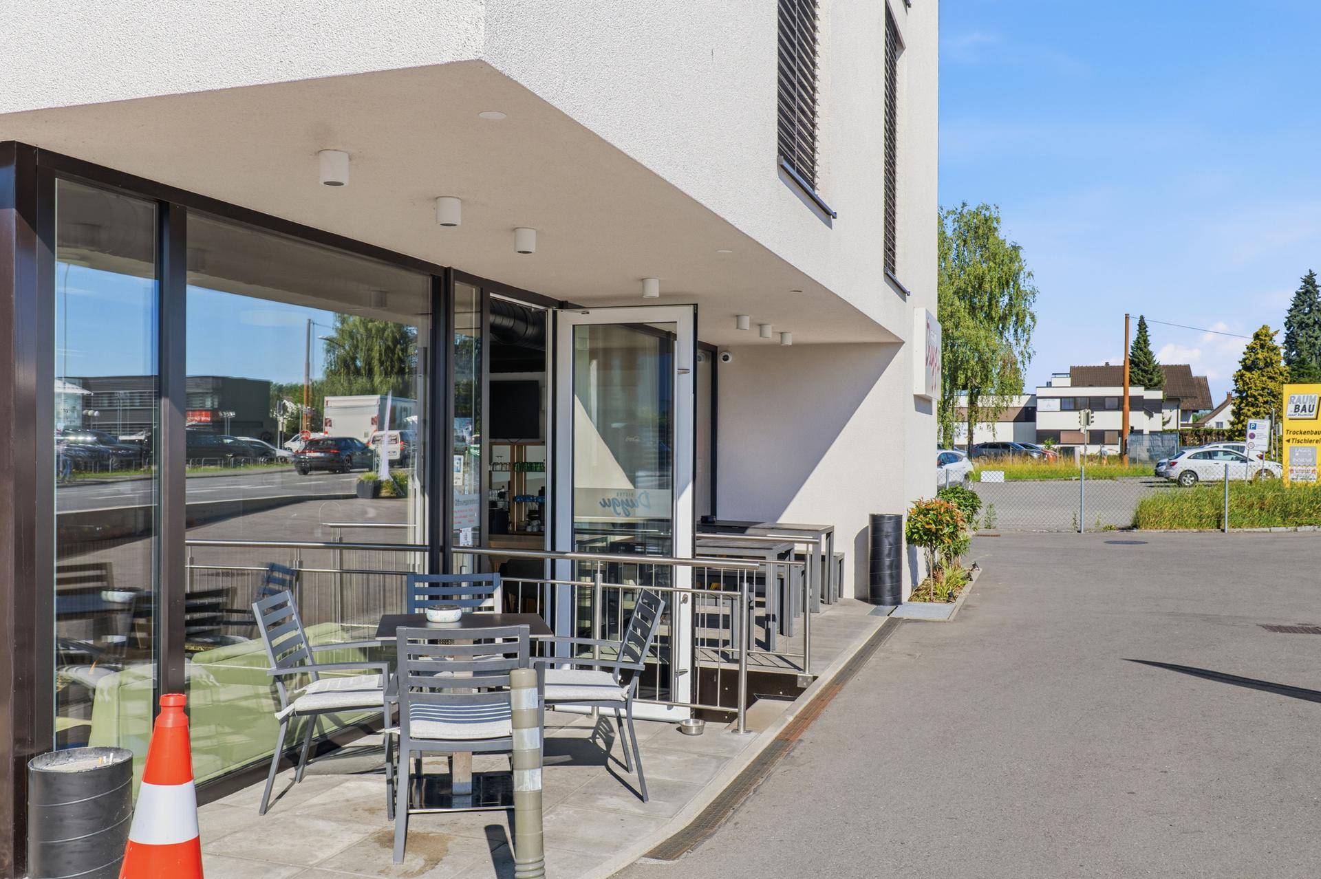 Außenterrasse des Bistros mit Tischen und Stühlen, direkt am Eingang des modernen Gebäudes.