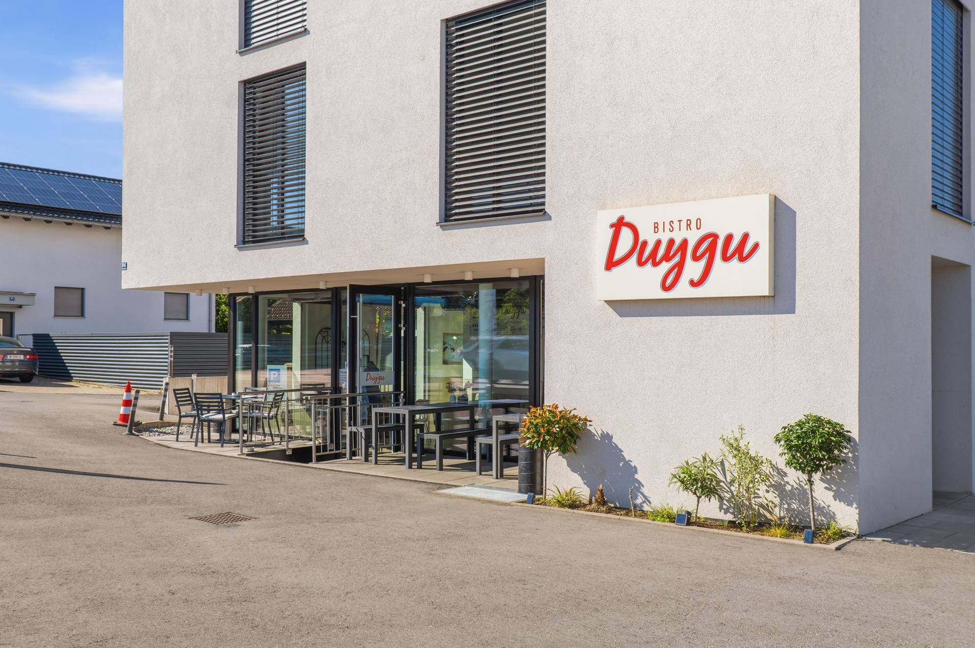 Modernes Geschäftsgebäude mit Bistro-Schild und Außenterrasse unter strahlend blauem Himmel.