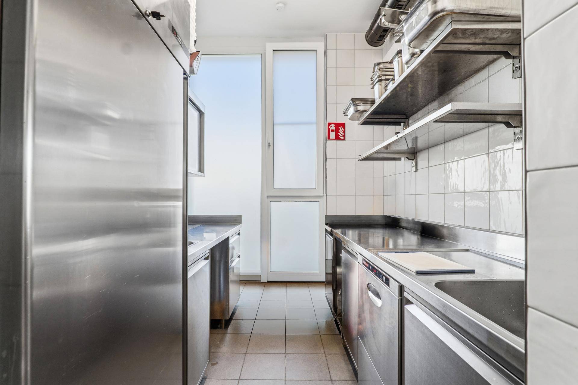 Professionelle Edelstahlküche mit Arbeitsflächen, Spülbecken und einem Fenster am Ende des Raumes.