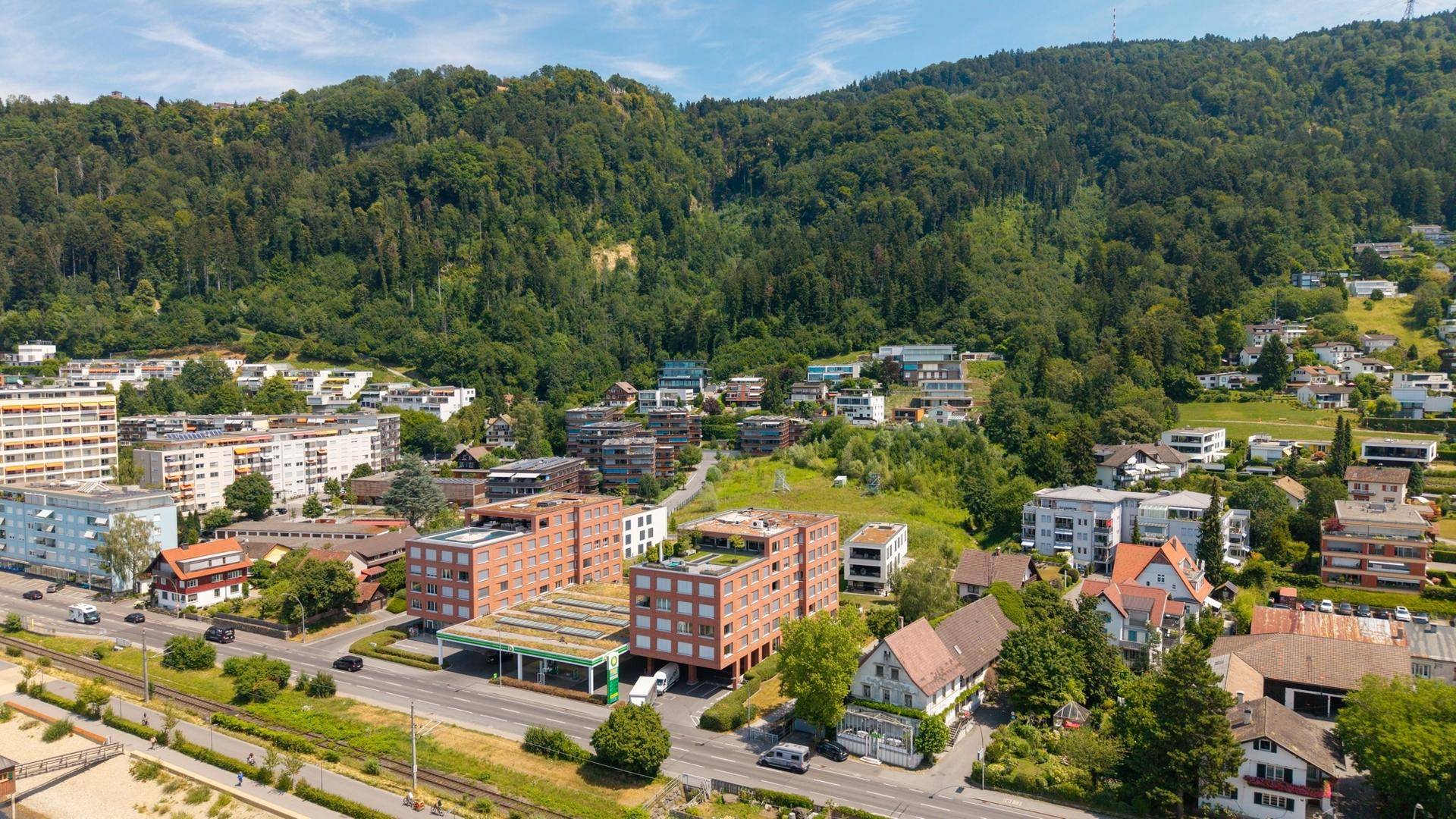 Luftaufnahme der Wohngebäude und der grünen Hügellandschaft im Hintergrund.