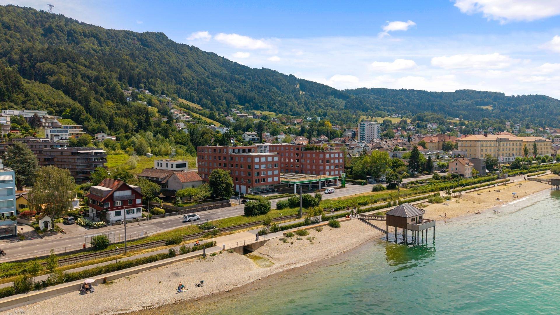 Weitwinkelaufnahme der Küstenlinie mit Gebäuden, Strand und grüner Landschaft.