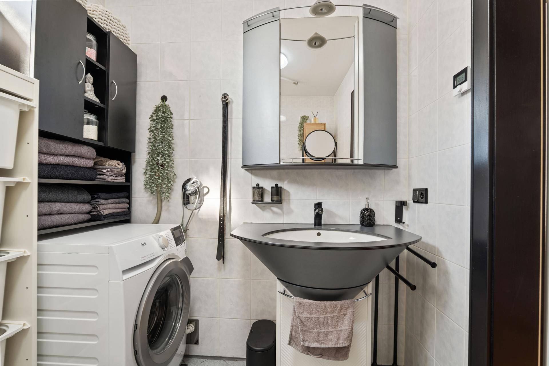 Badezimmer mit modernem Waschbecken, Spiegelschrank und integrierter Waschmaschine.
