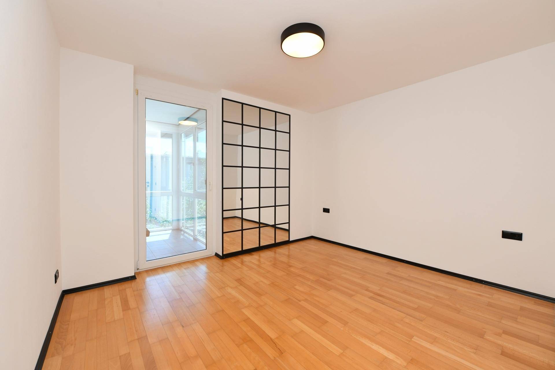 Helles Zimmer mit Holzboden und Zugang zu einem verglasten Wintergarten.
