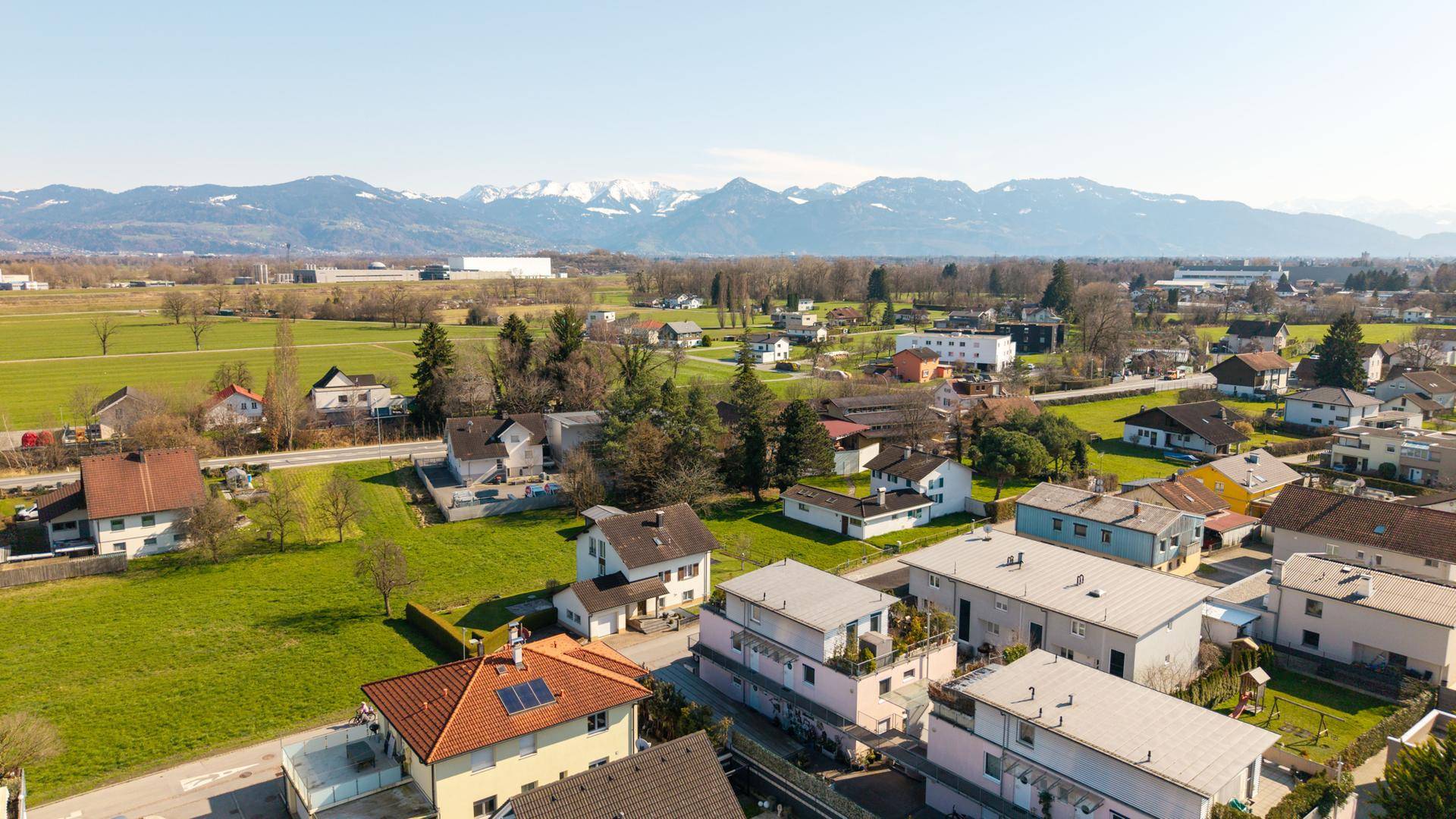 Luftaufnahme der ländlichen Wohngegend mit schneebedeckten Bergen am Horizont.