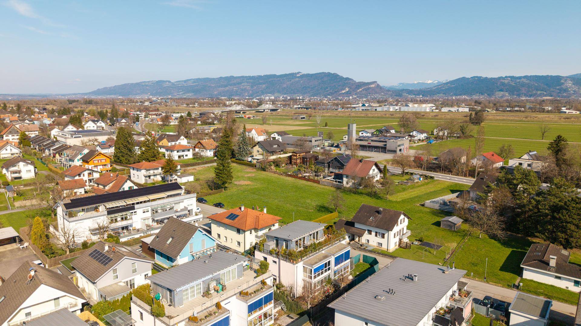 Luftaufnahme der Wohngegend mit grünen Feldern und Bergen im Hintergrund.