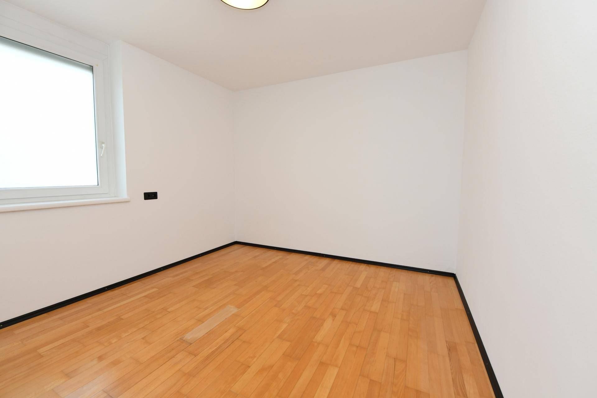 Geräumiges Schlafzimmer mit Holzboden und Fenster, ideal für persönliche Gestaltung.
