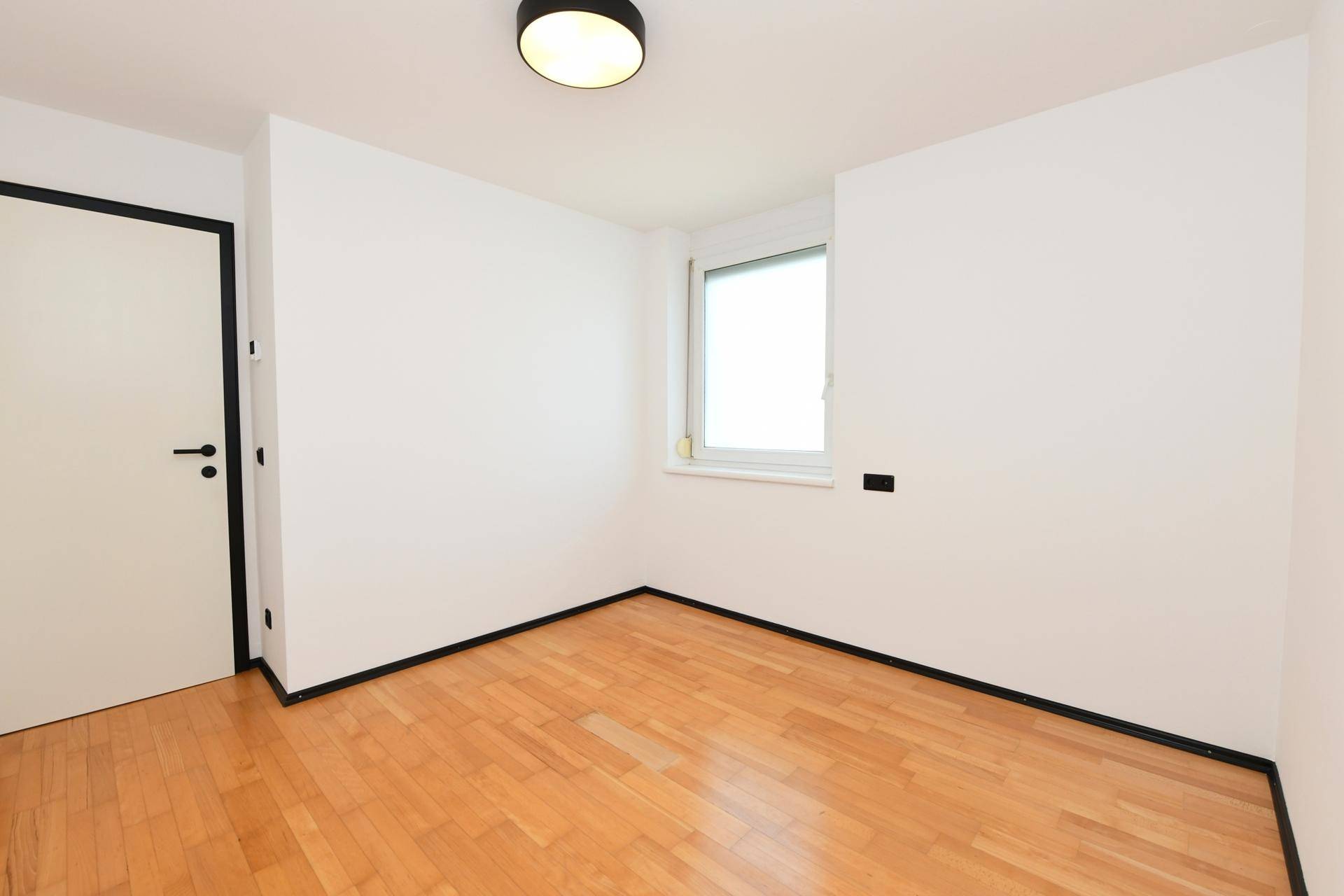 Helles Schlafzimmer mit Holzboden und Fenster, bereit zur individuellen Einrichtung.