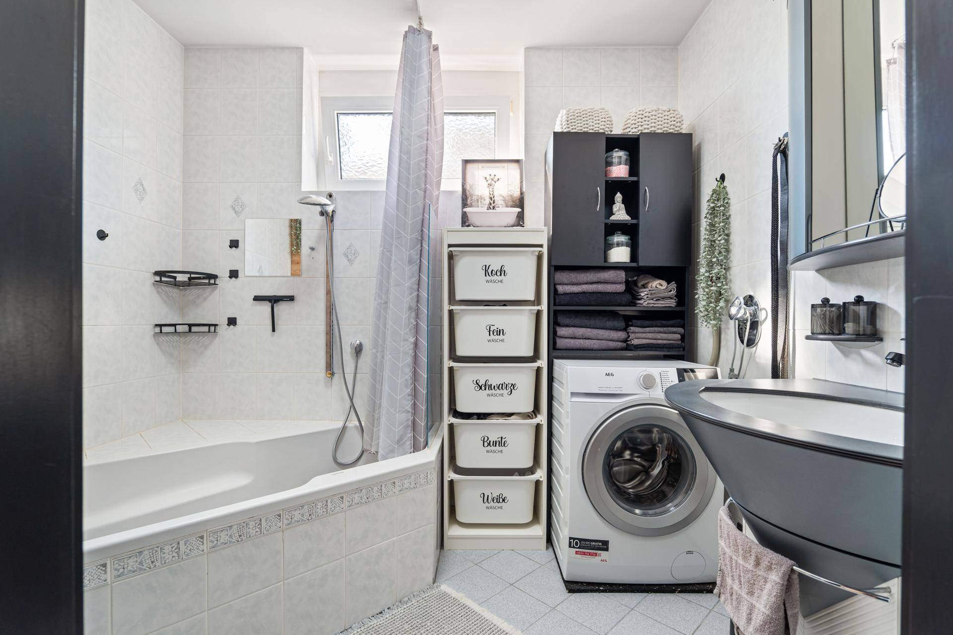 Funktionales Badezimmer mit Badewanne, Waschmaschine und hellen Fliesen.