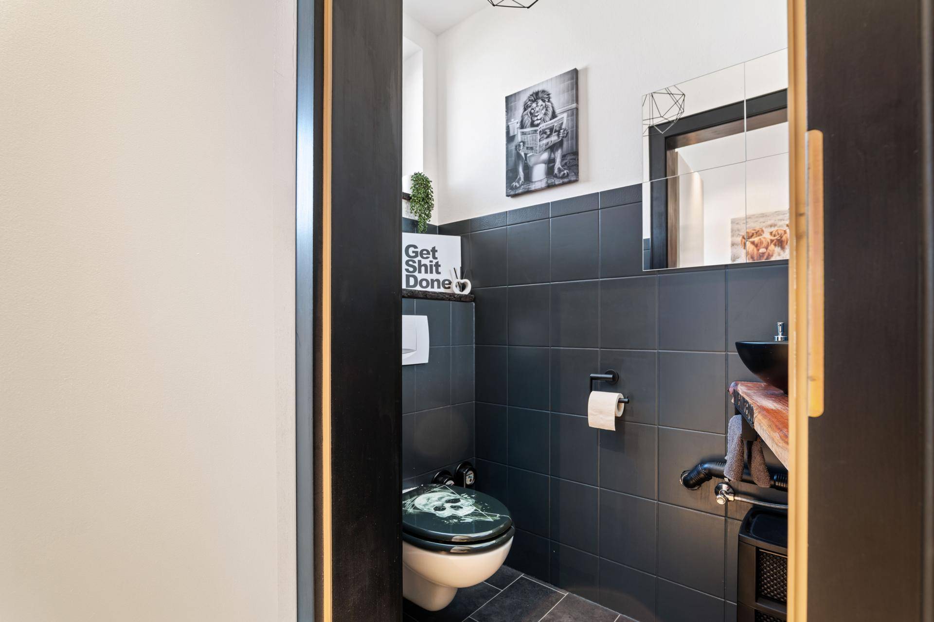 Modernes Gäste-WC mit dunklen Fliesen, Wand-WC und kleinem Waschbecken.