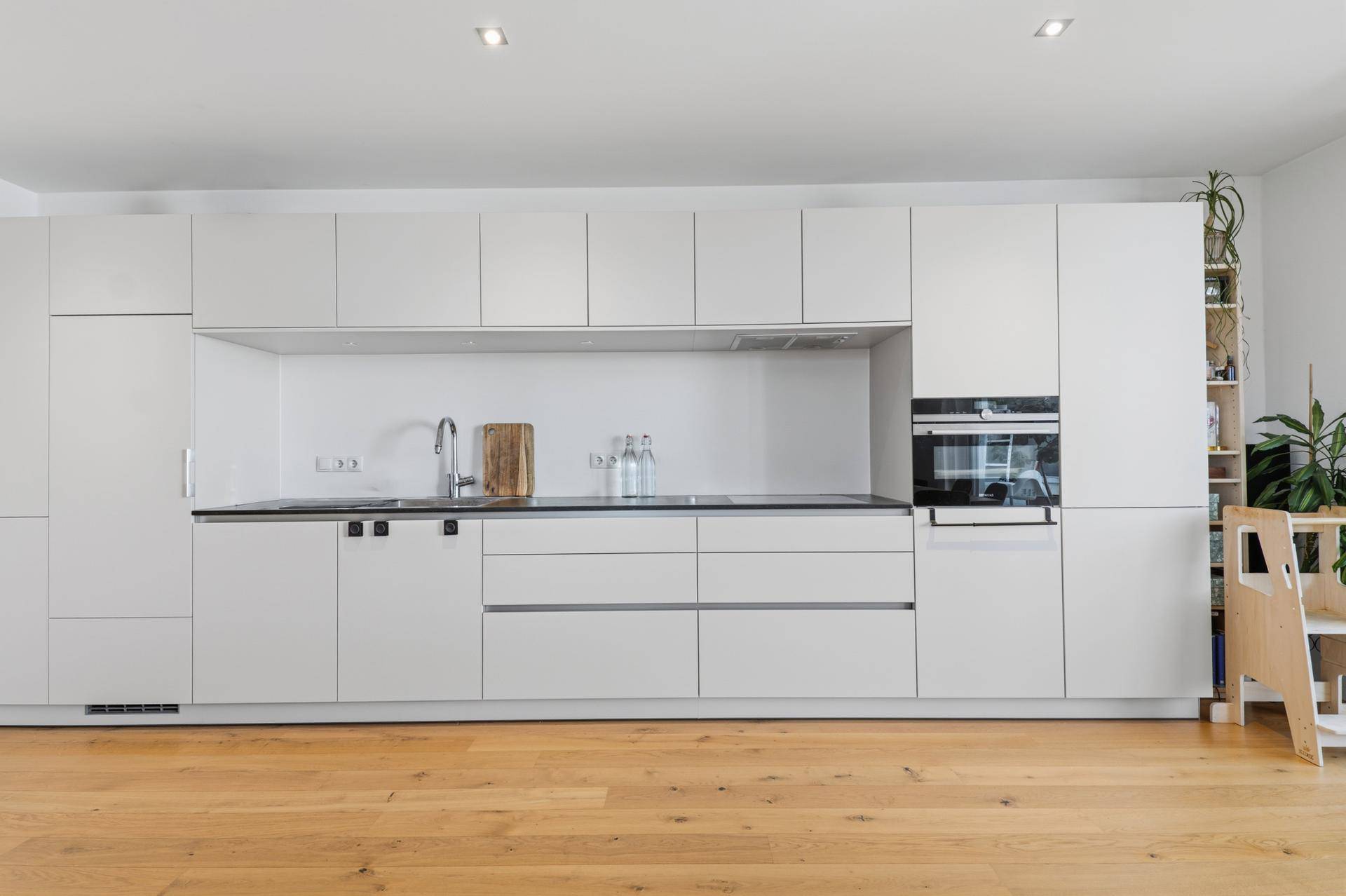 Moderne, minimalistische Einbauküche in Weiß mit integrierten Geräten und Holzboden.