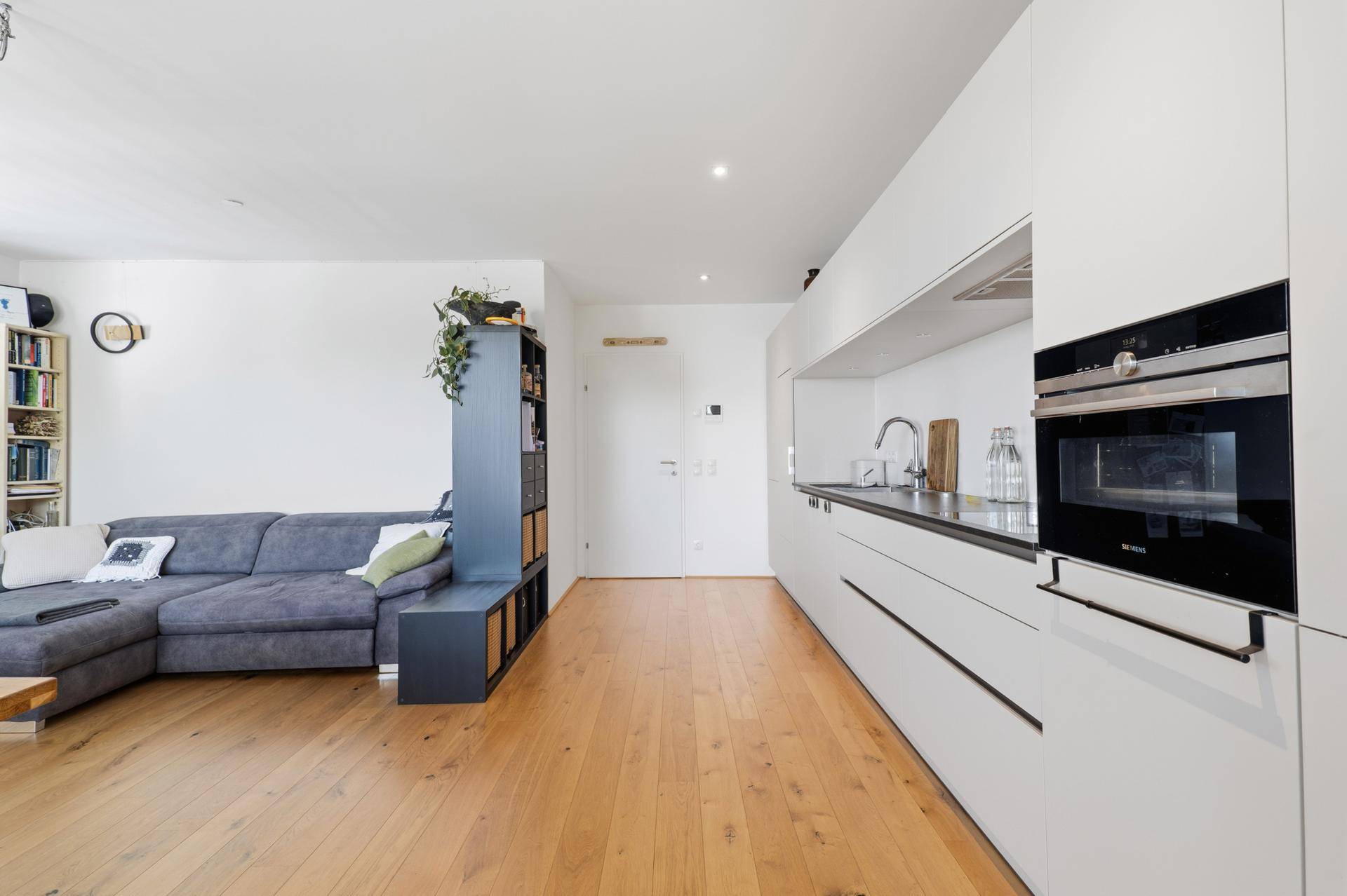 Heller Wohnbereich mit moderner Küche, Sofa und Holzboden.