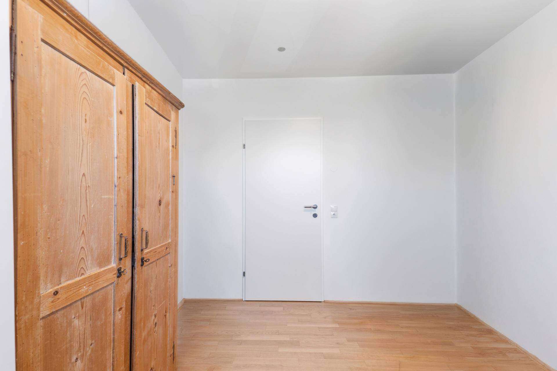 Schlafzimmer mit Holzboden und einem großen Holzschrank.