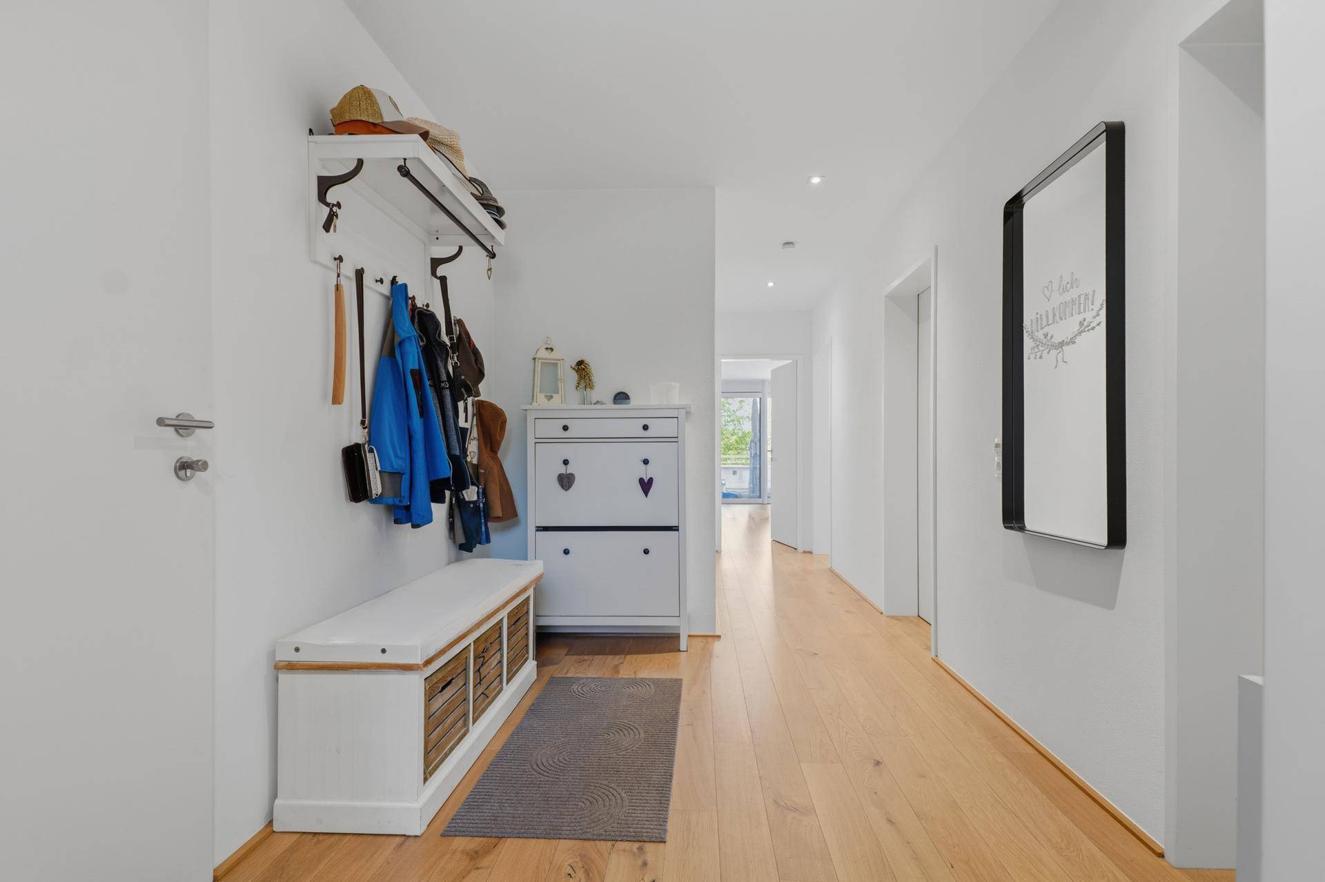 Heller Flur mit Holzboden, Garderobe und Spiegel.