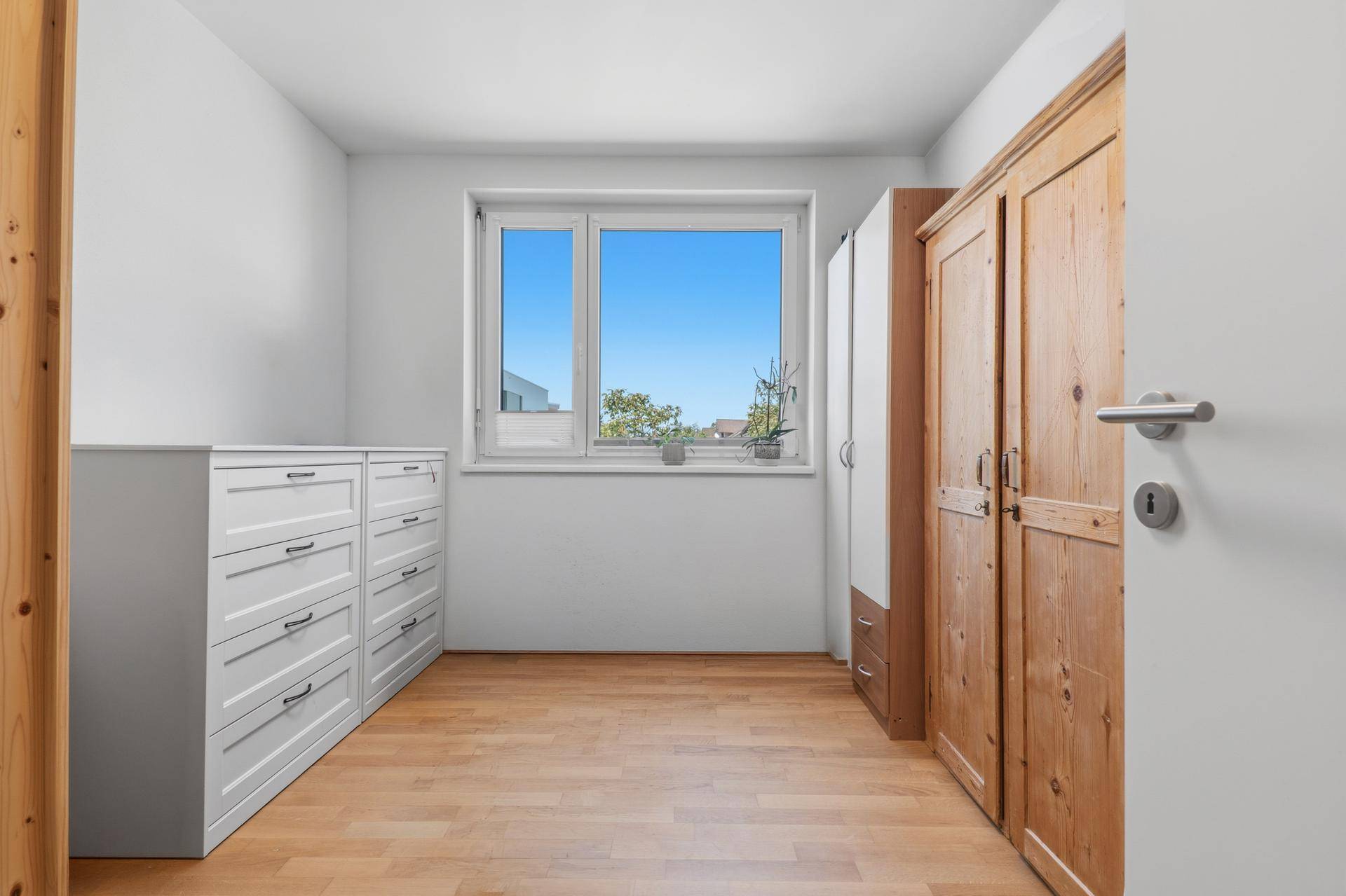 Helles Schlafzimmer mit Holzboden, Fenster und Schränken.